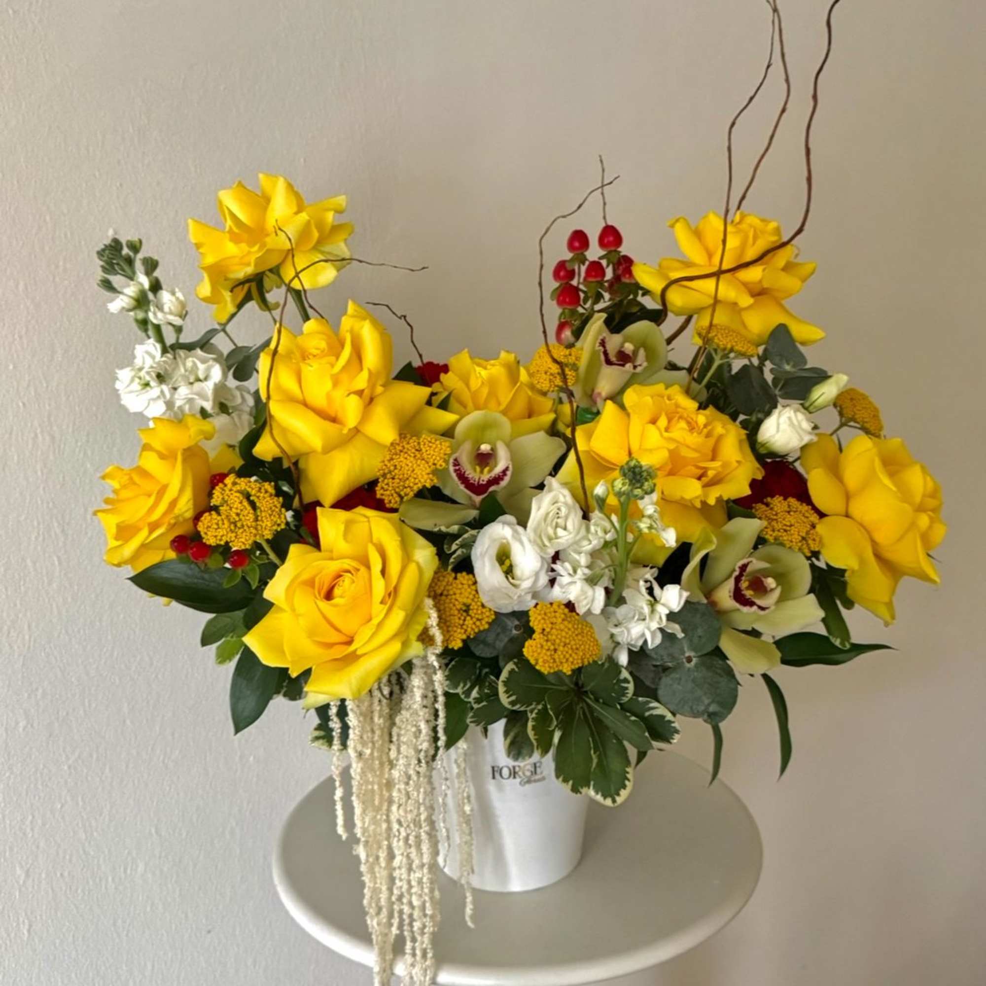 A bright and elegant arrangement featuring vibrant yellow roses, orchids, seasonal blooms