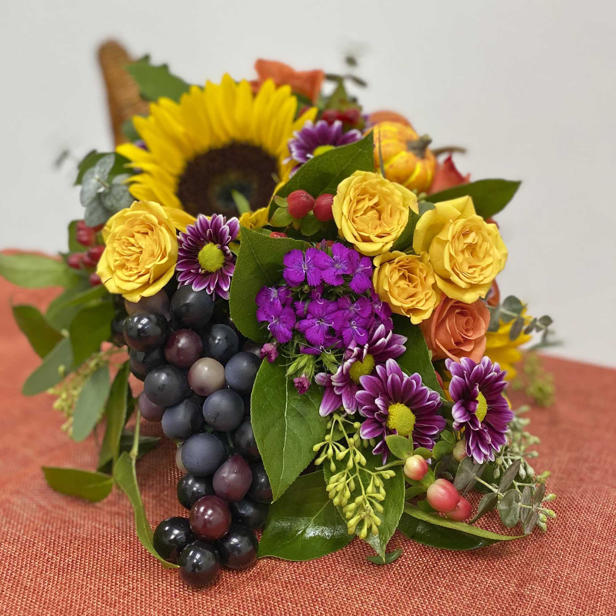 Mixed bouquet with yellow roses, sunflowers, purple daisies, and dark grapes
