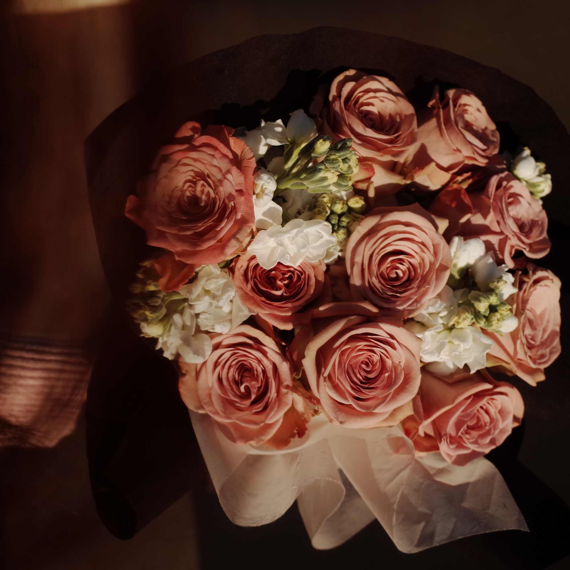 Bouquet of pink roses with small white flowers wrapped in dark paper