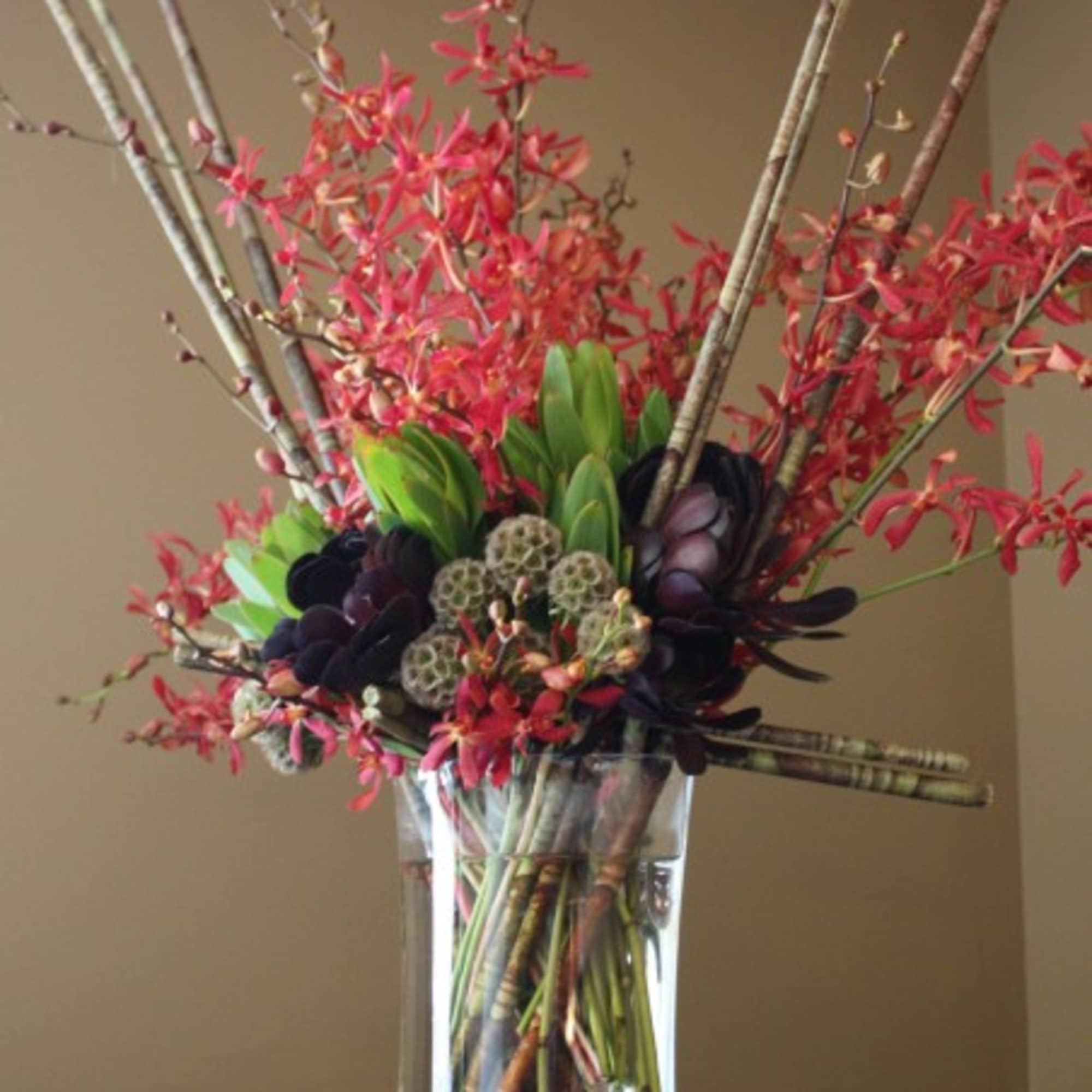 Tall floral arrangement with red blooms in a clear glass vase