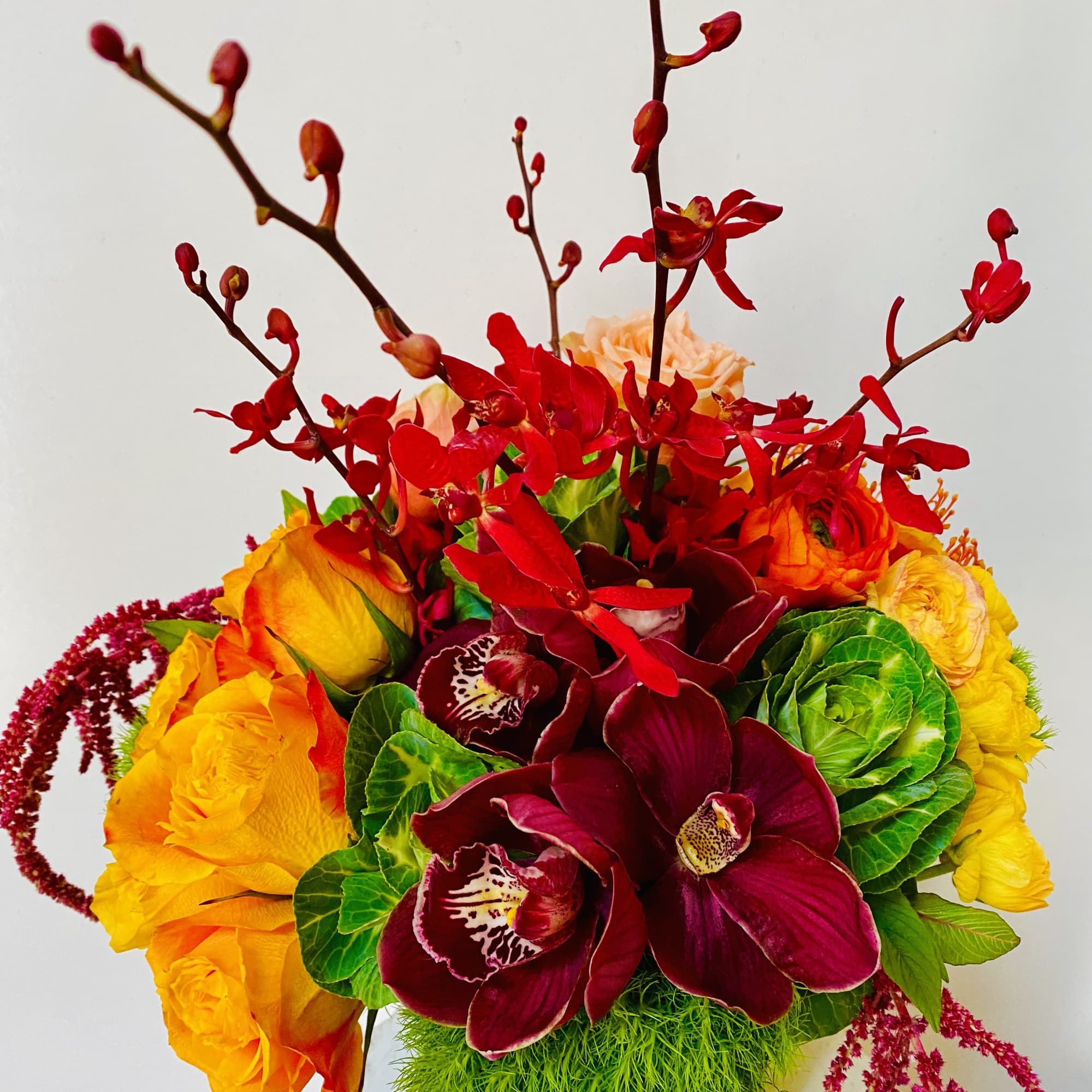 Bright bouquet of red orchids, yellow roses, and green blooms in a glass vase
