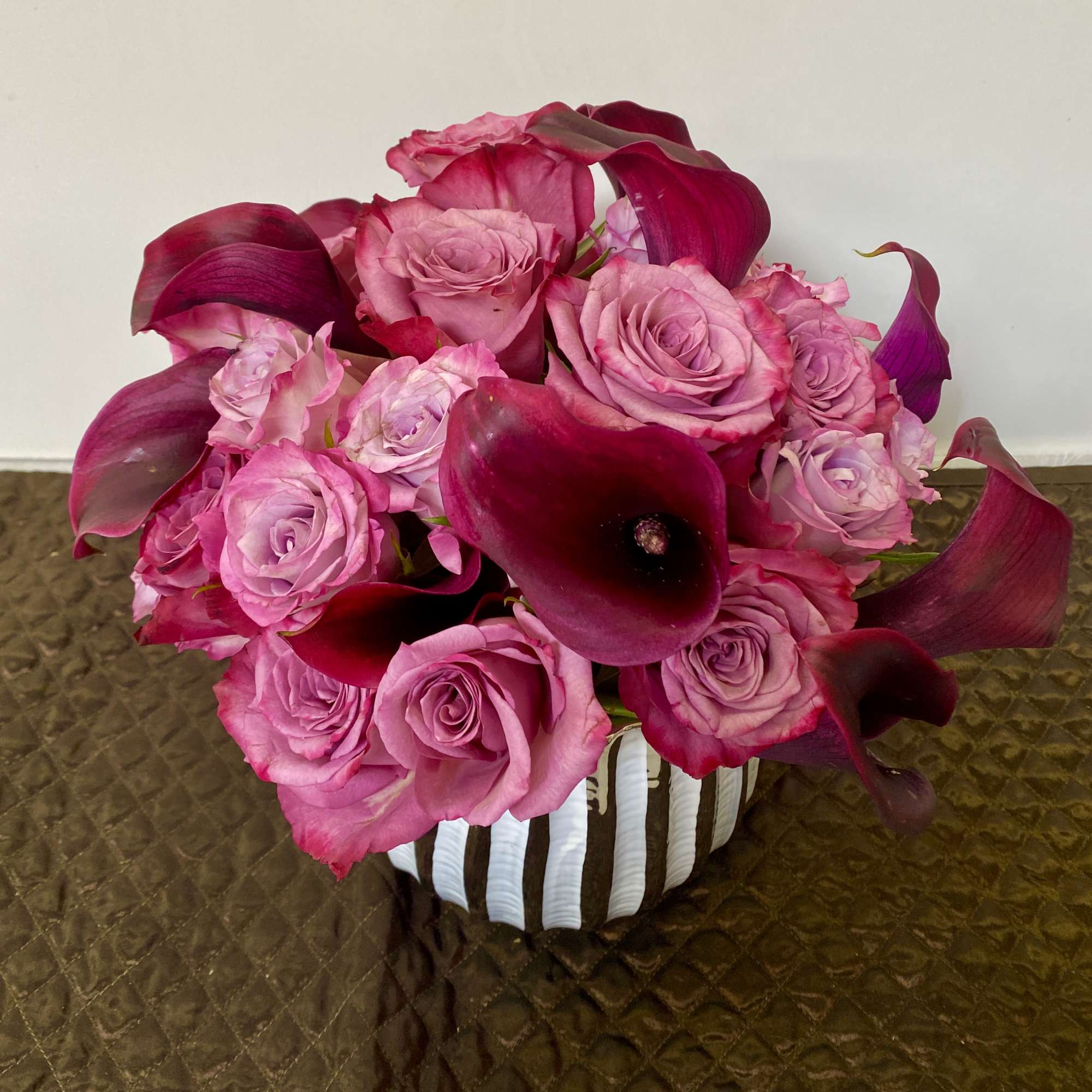 Pink roses and dark magenta calla lilies in a striped vase