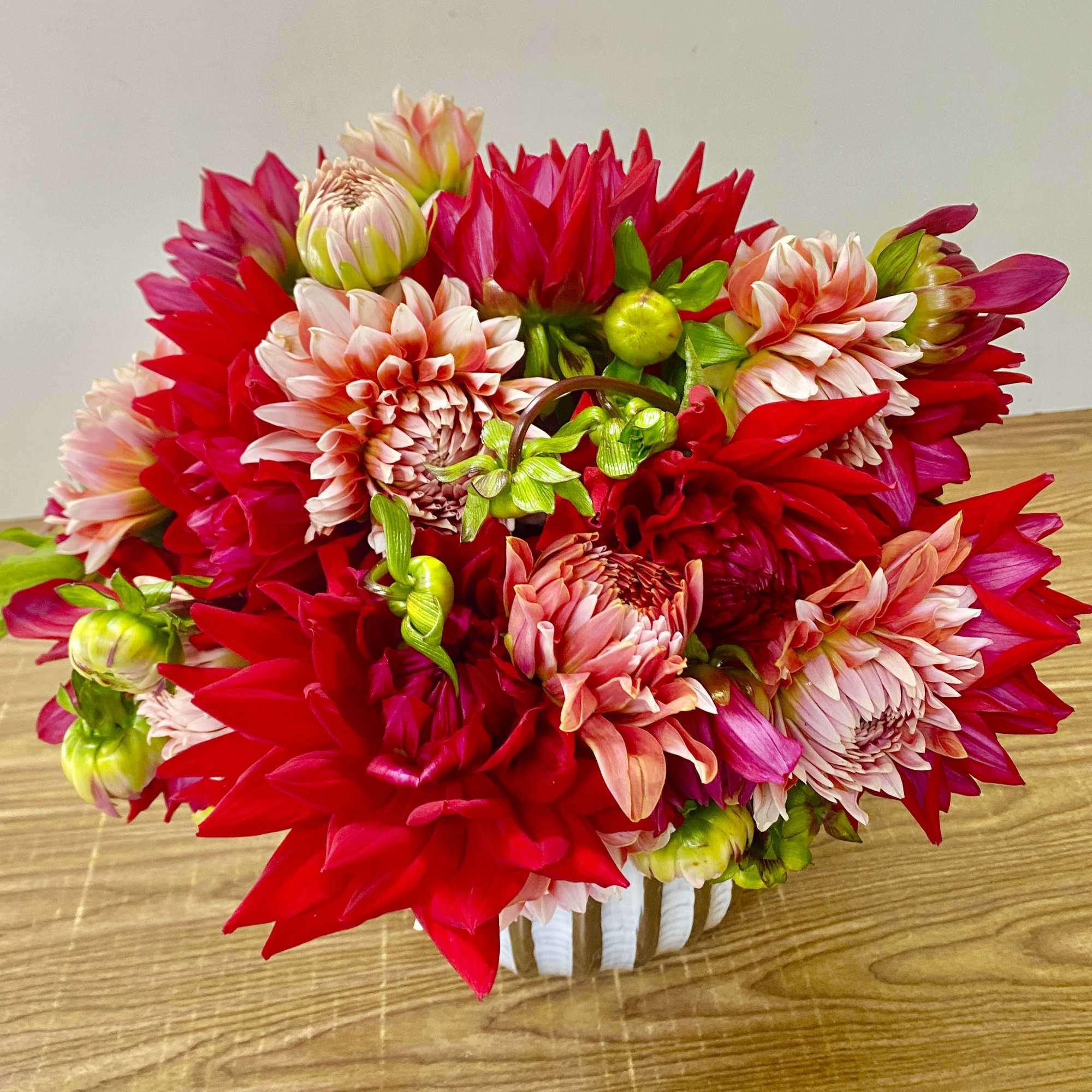 Bright red and pink dahlia bouquet in a white container