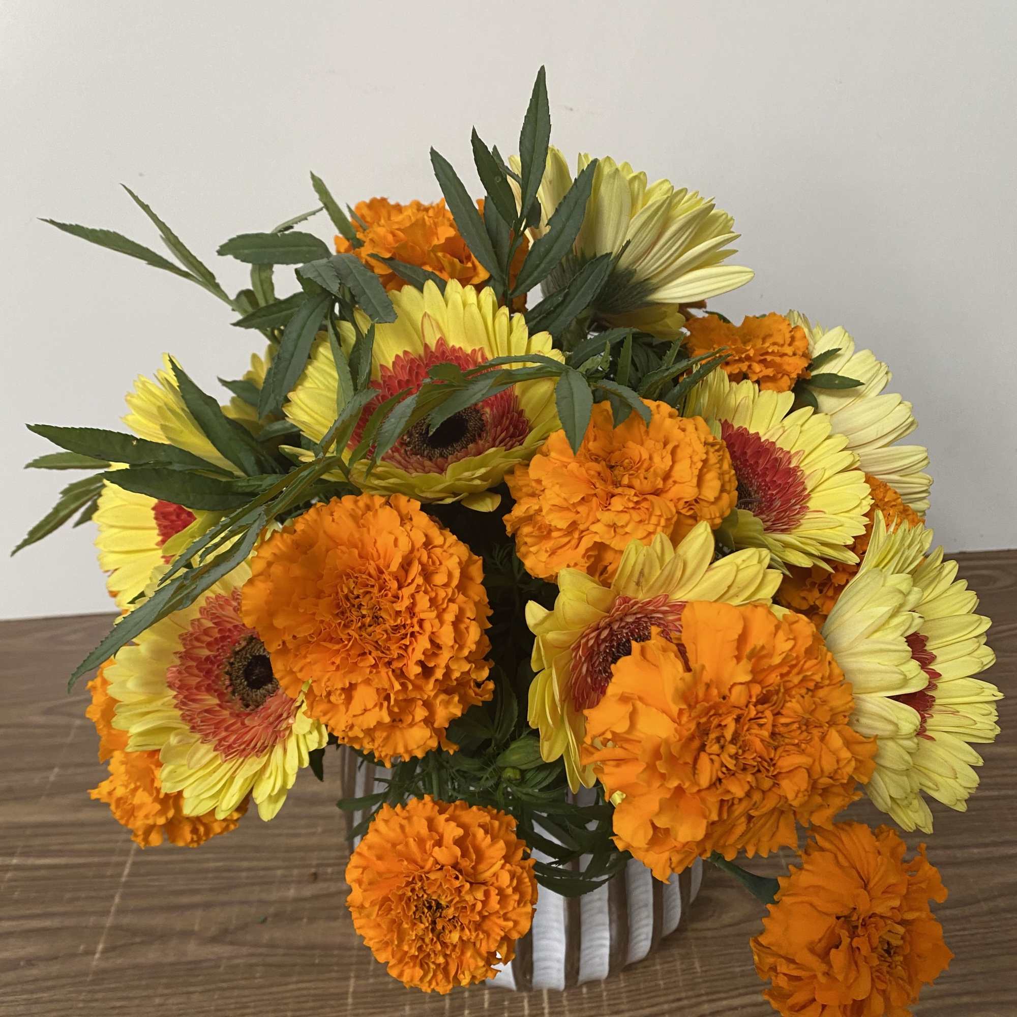 Bouquet of yellow gerbera daisies and orange marigolds in a white vase