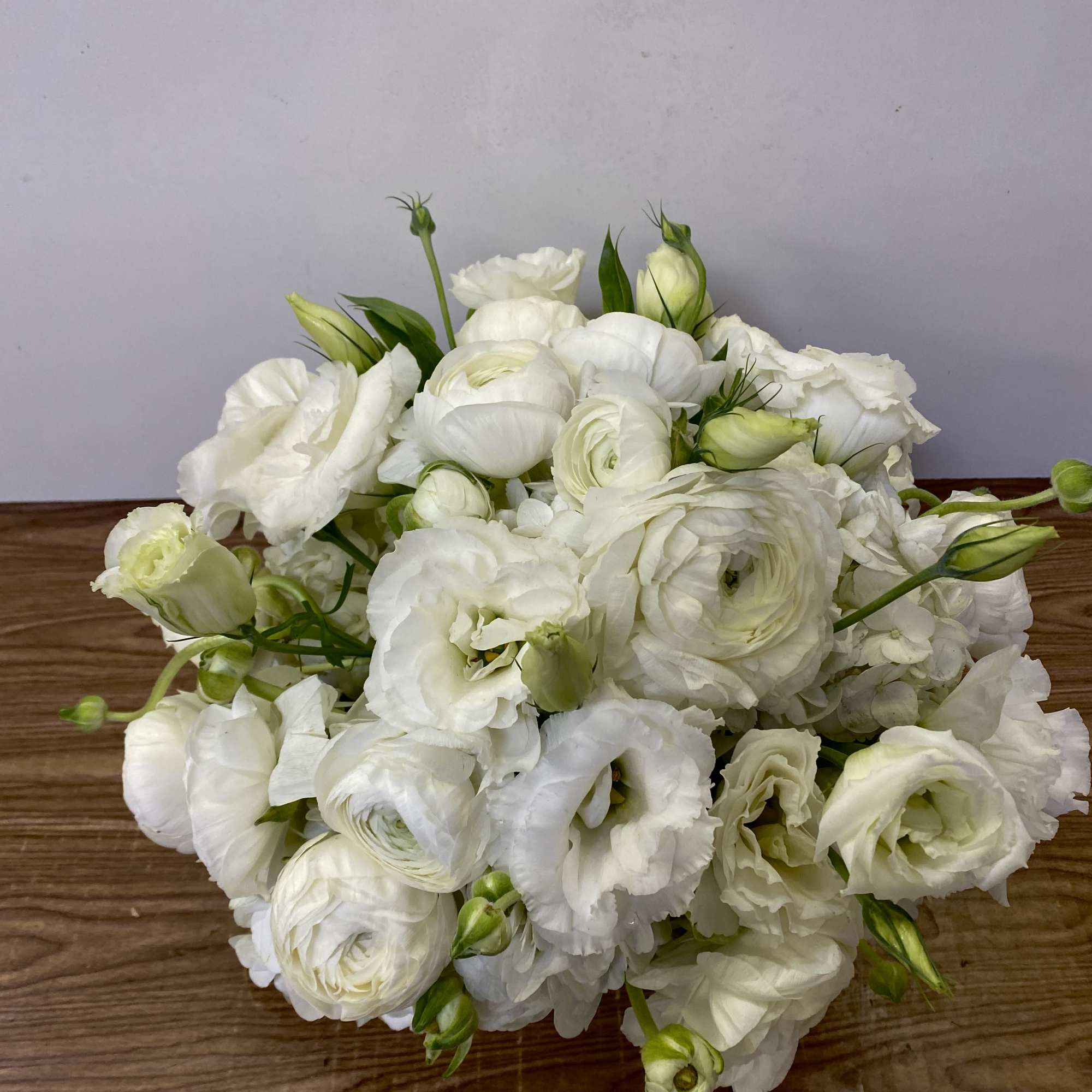 White bouquet of ranunculus and lisianthus on a wooden surface