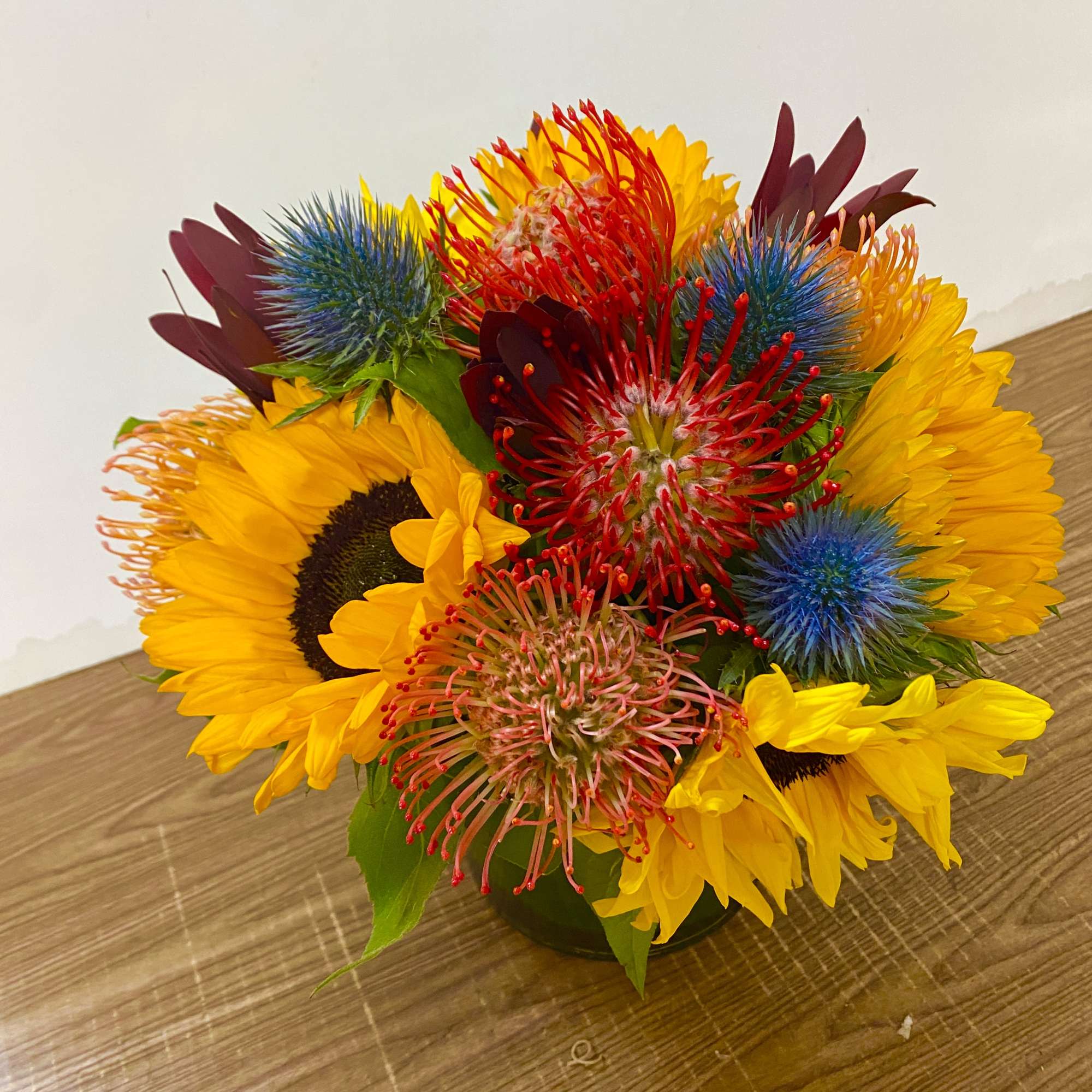 Bright mixed bouquet with sunflowers and spiky tropical blooms in a low vase