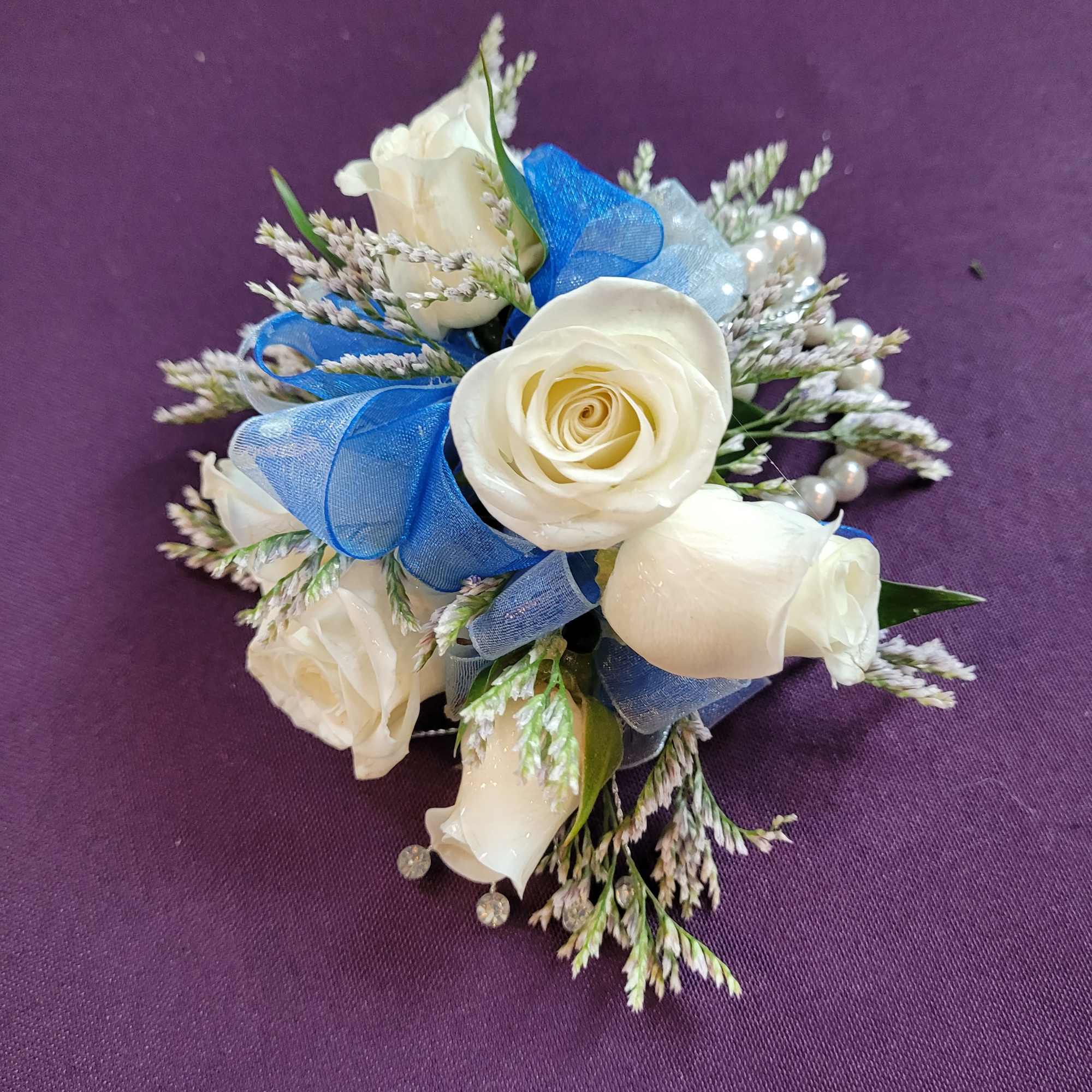 White rose corsage with blue ribbon on a purple background