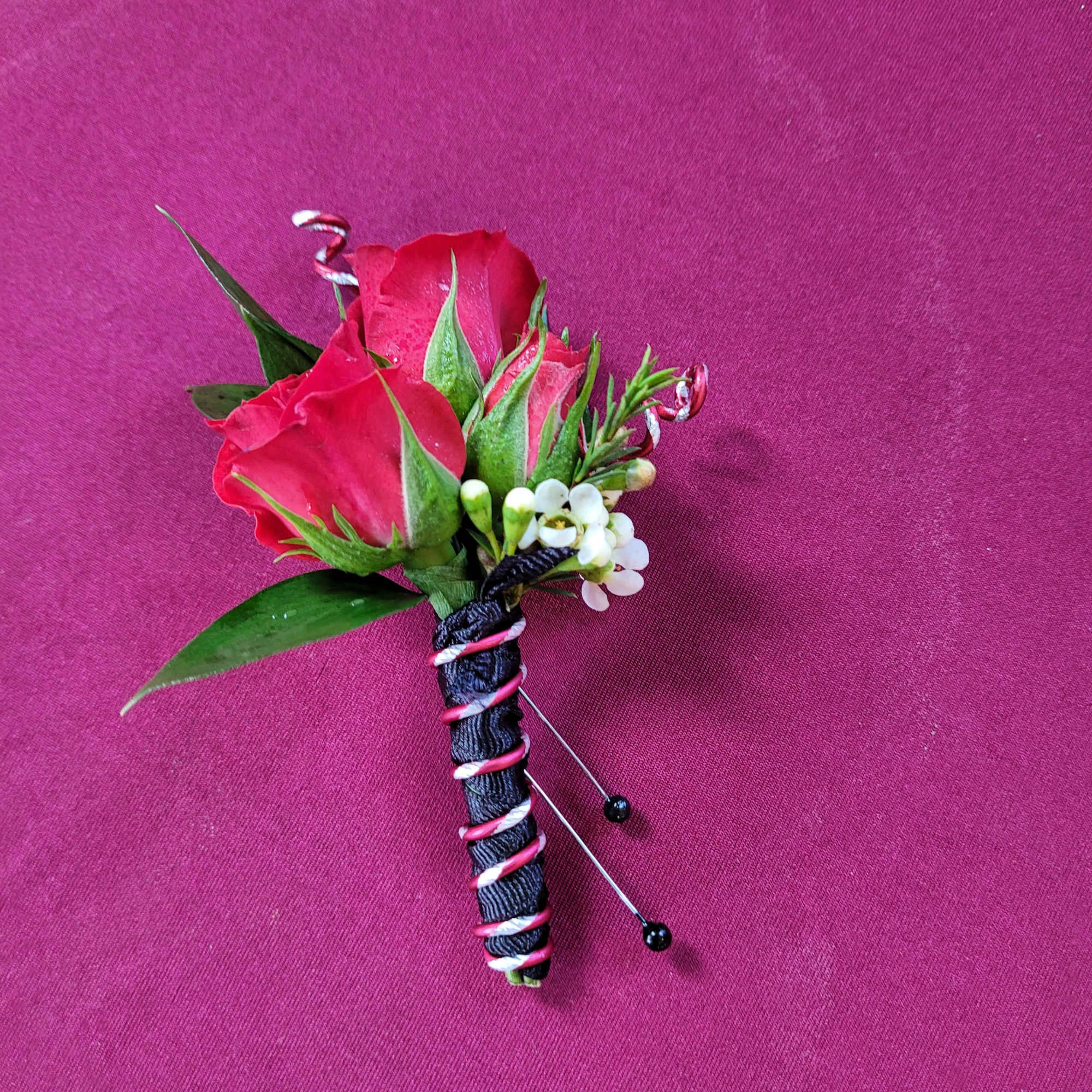 Boutonniere with red roses and small white flowers on a pink background