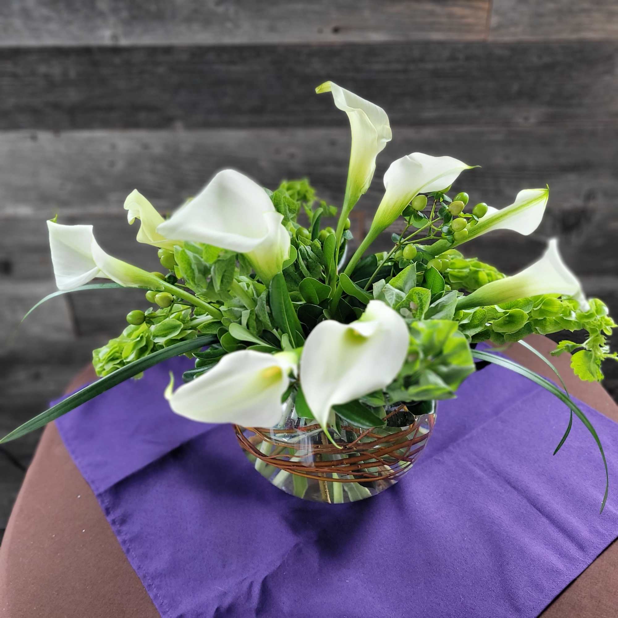 White calla lilies arranged in a clear glass bowl with green accents