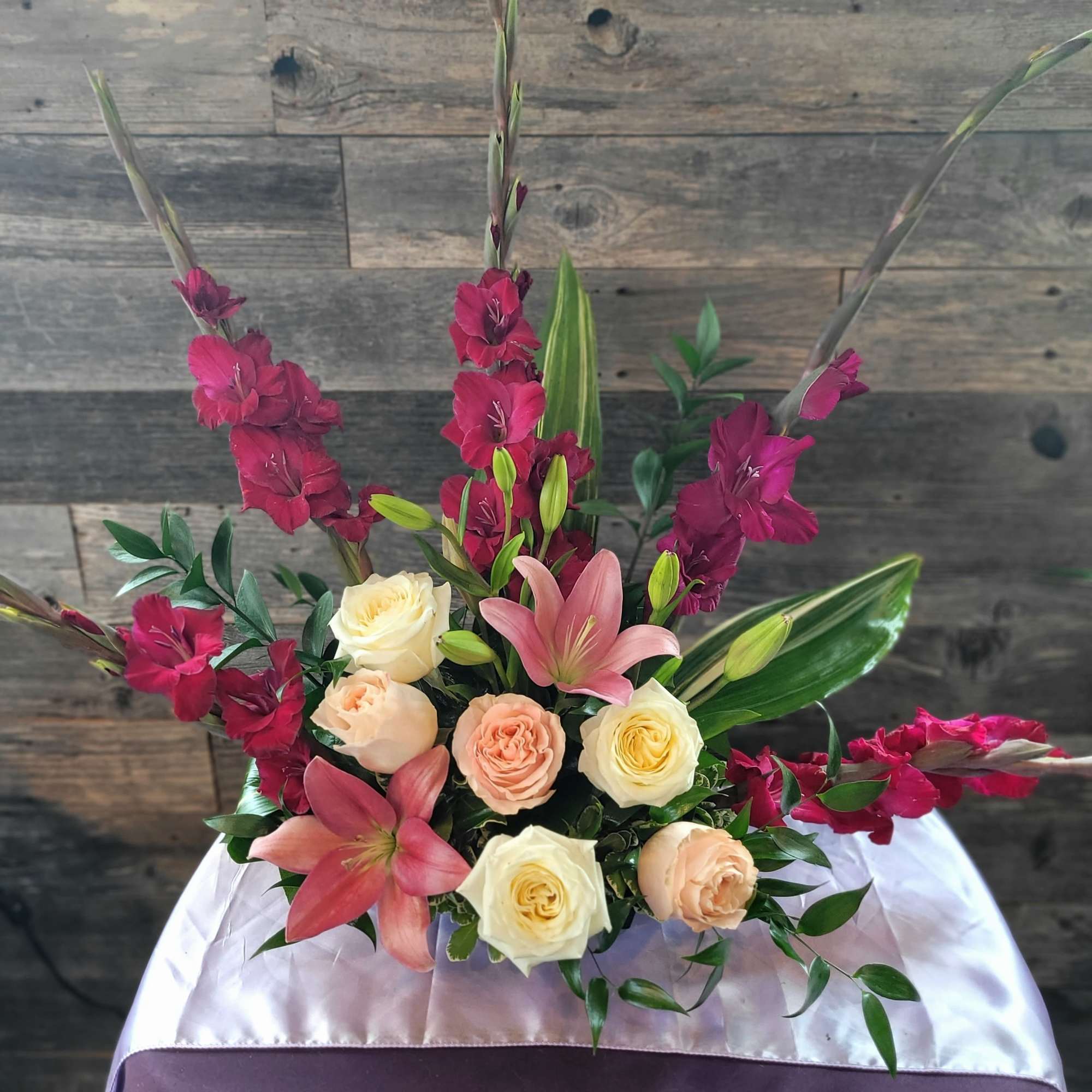 A layered upright bouquet of soft pink lilies, cream-to-peach roses, and tall