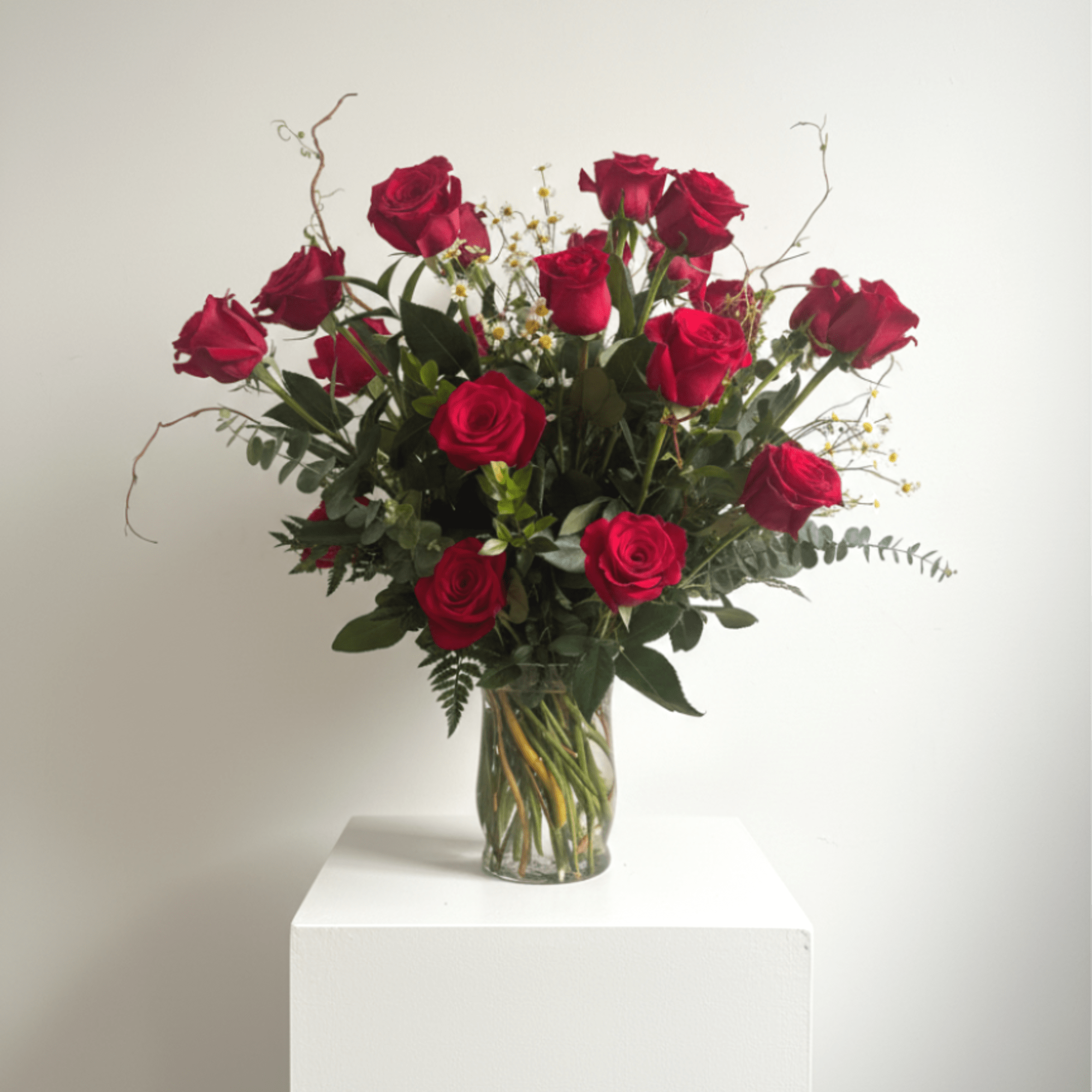 Tall arrangement of red roses in a clear glass vase on a white pedestal