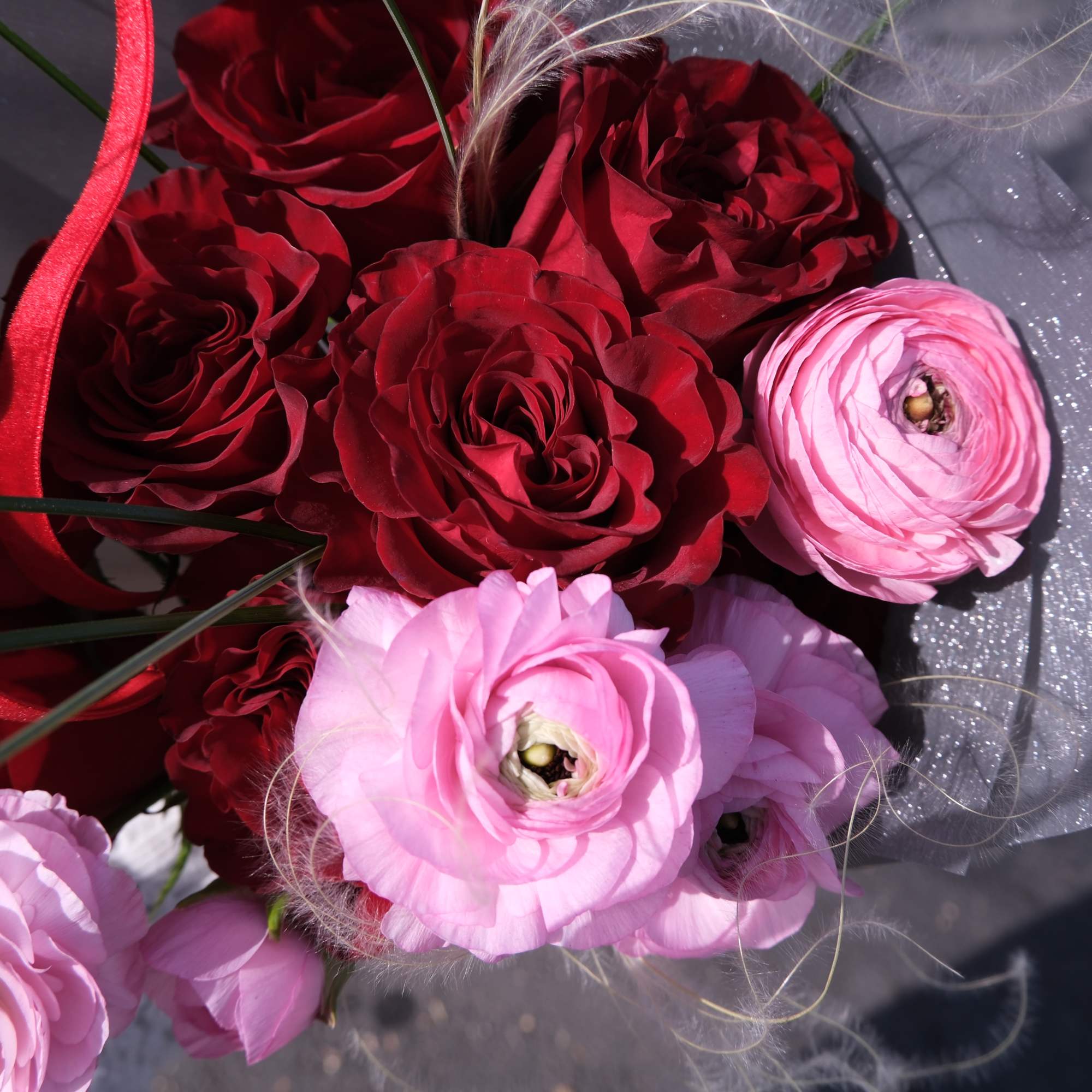 Bouquet of red roses and pink ranunculus wrapped in gray paper