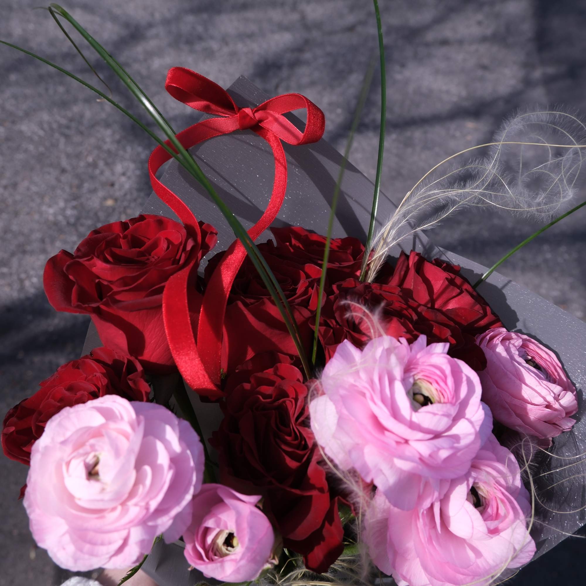 Bouquet of red roses and pink ranunculus with a red ribbon wrap