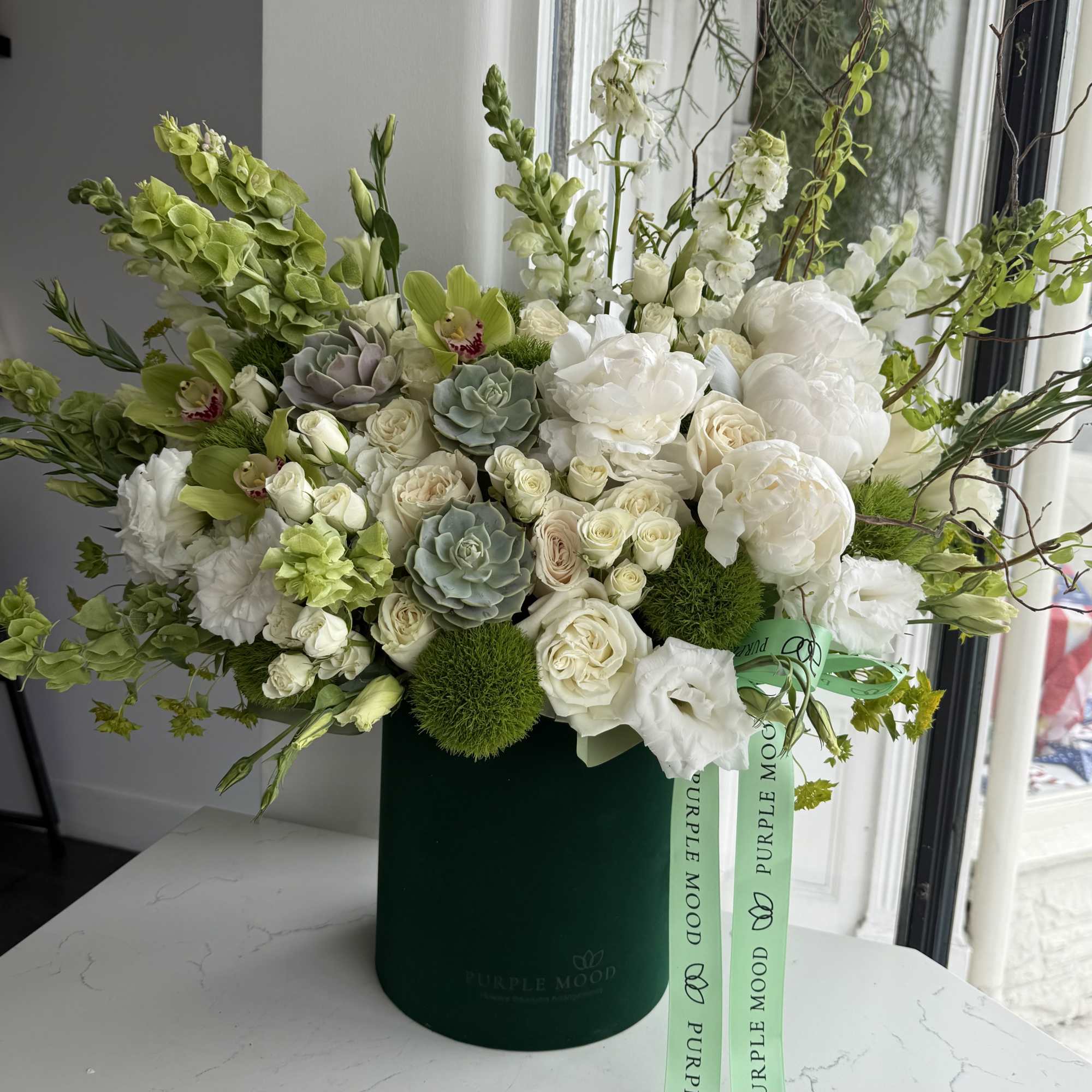 White and green floral arrangement in a dark green box with ribbon