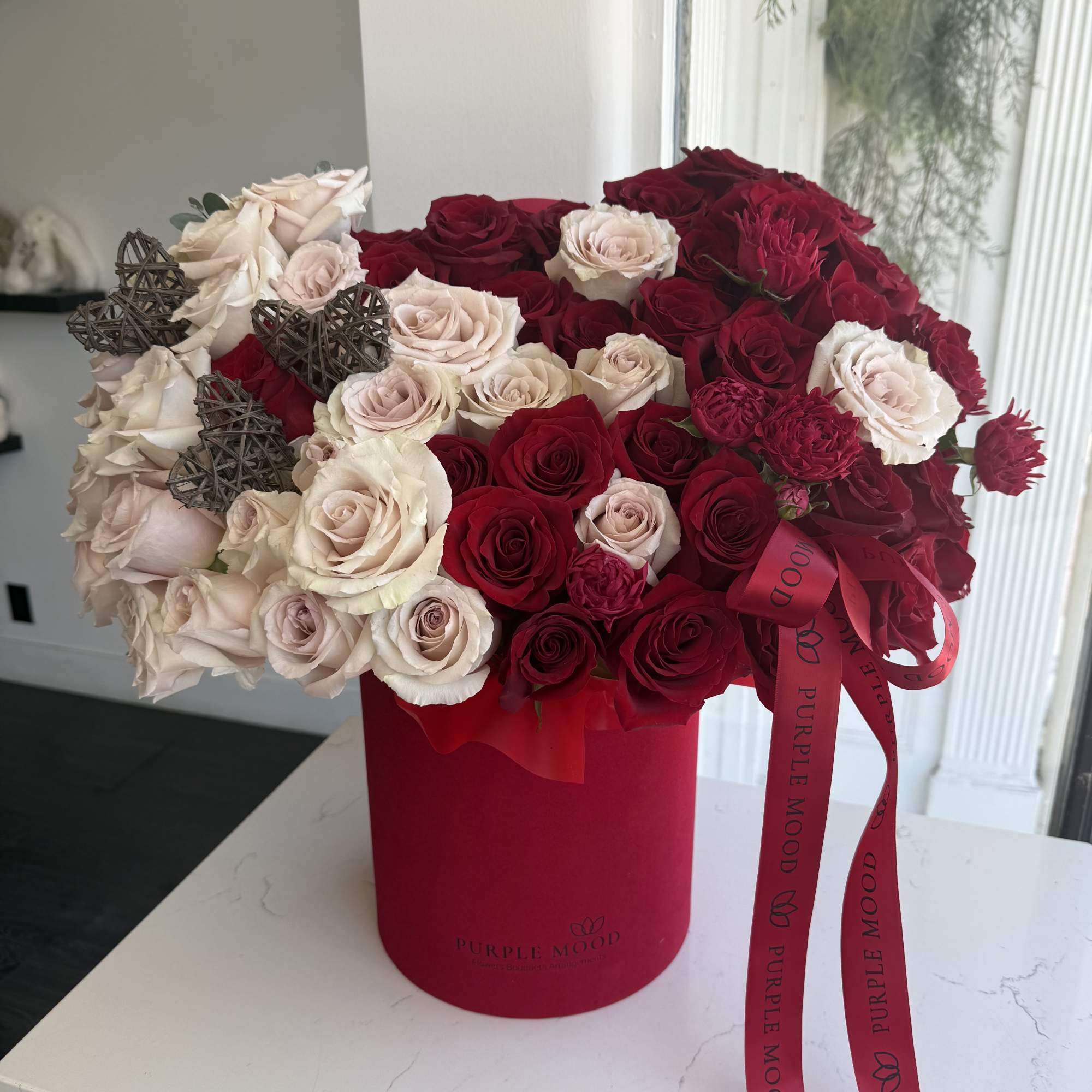 Red and blush roses arranged in a red hatbox with ribbon.