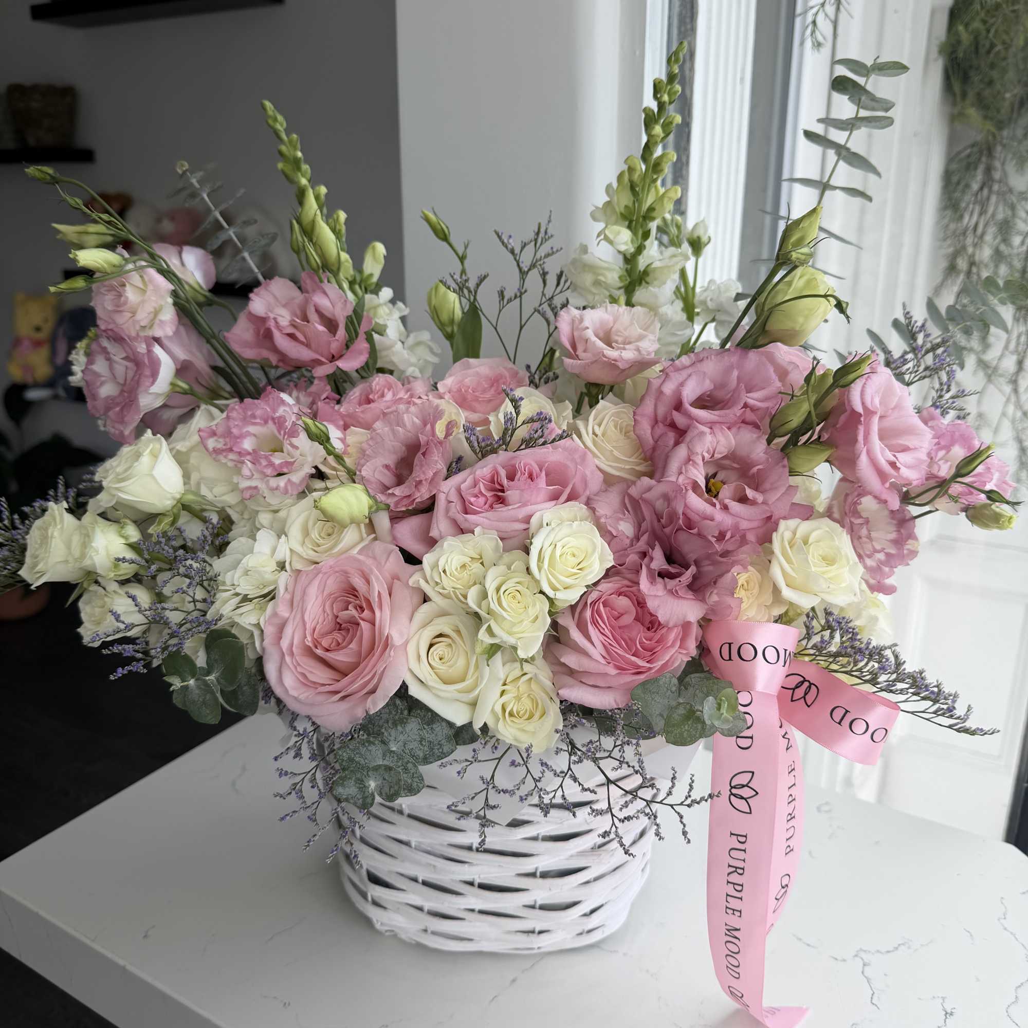 Pink and white flower arrangement in a white basket with a pink ribbon