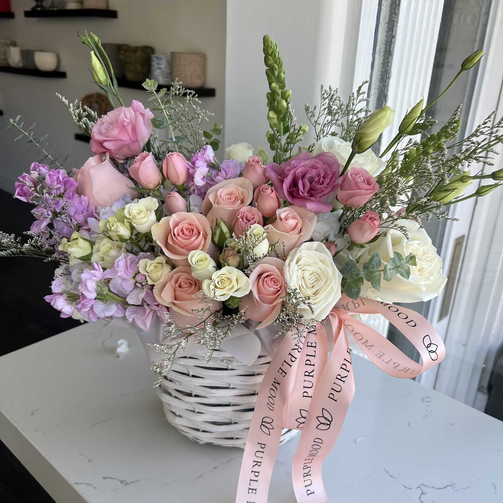 Pink and white rose bouquet in a white basket with a pink ribbon