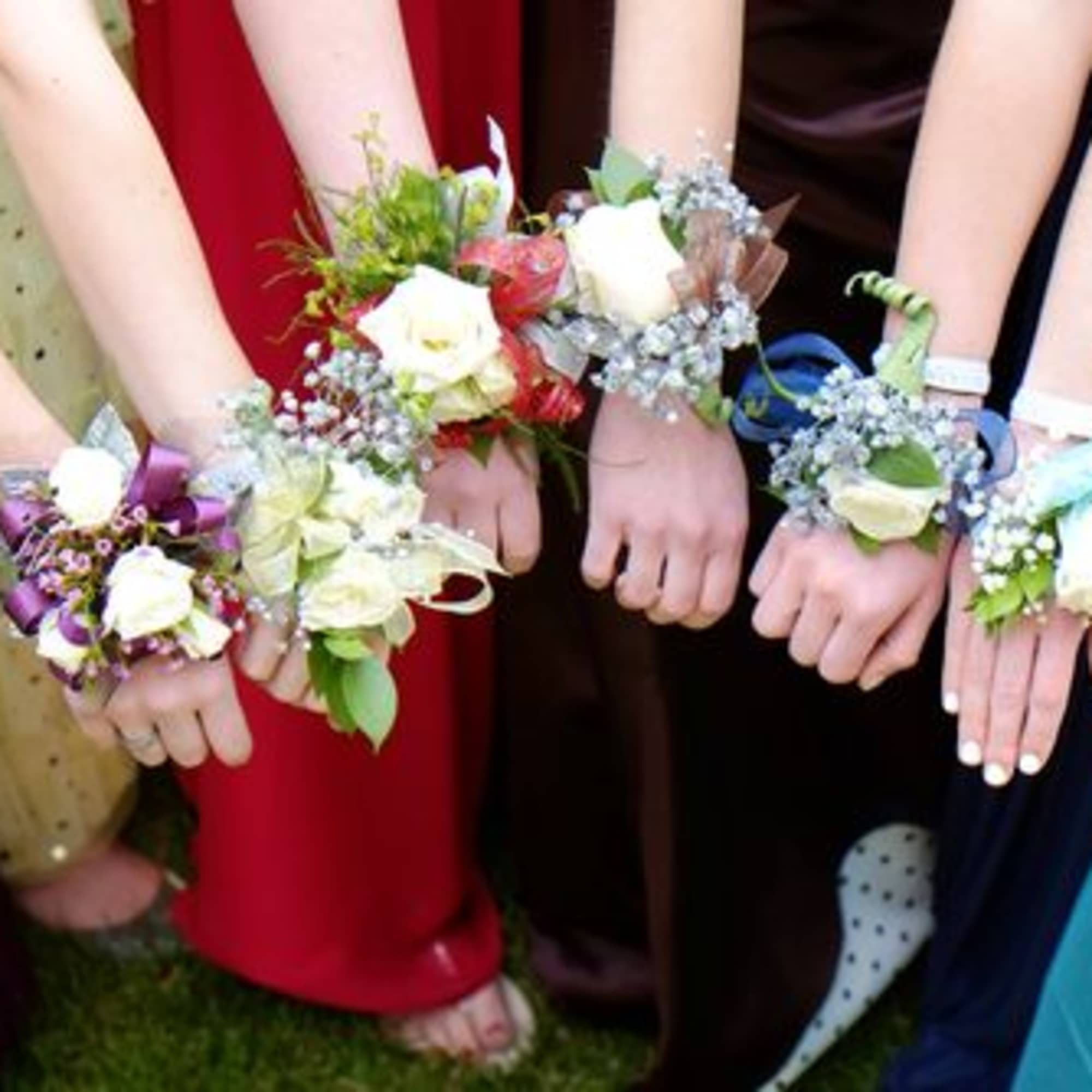 Group of hands wearing floral wrist corsages with white roses and ribbon