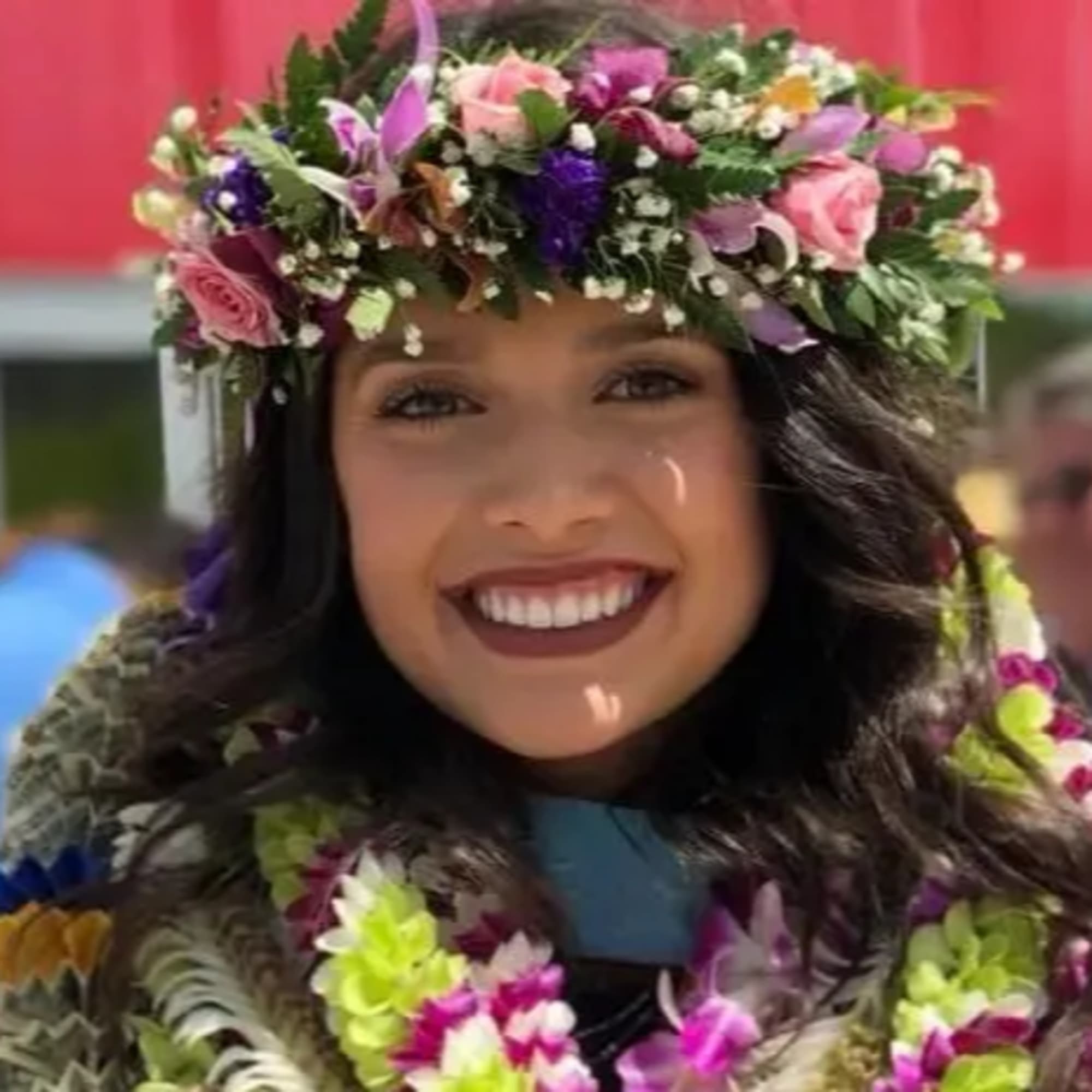 Floral crown of pink and purple flowers with matching leis worn by a smiling person.