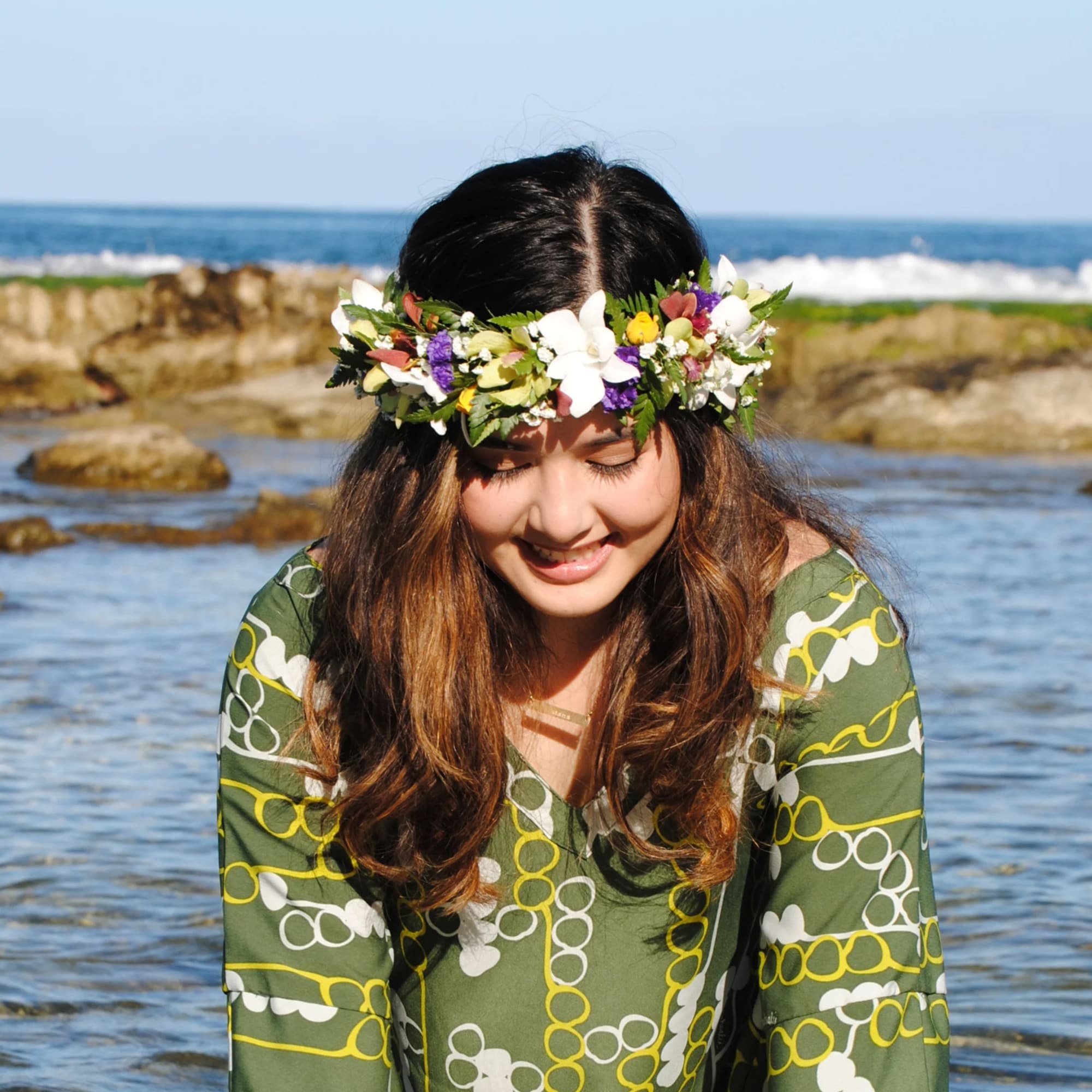 Woman wearing a white, yellow, and purple flower crown by the ocean