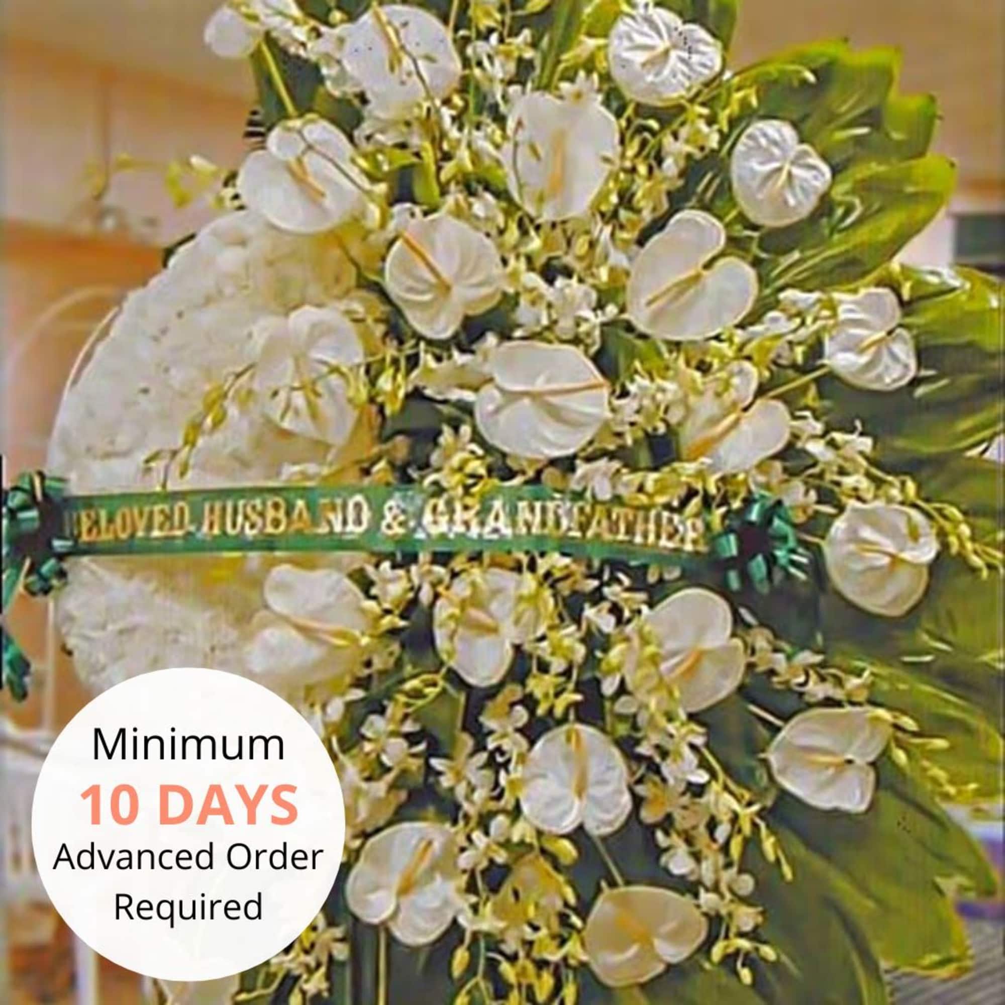 Tall white funeral easel spray with white blooms and ribbon reading Beloved Husband & Grandfather