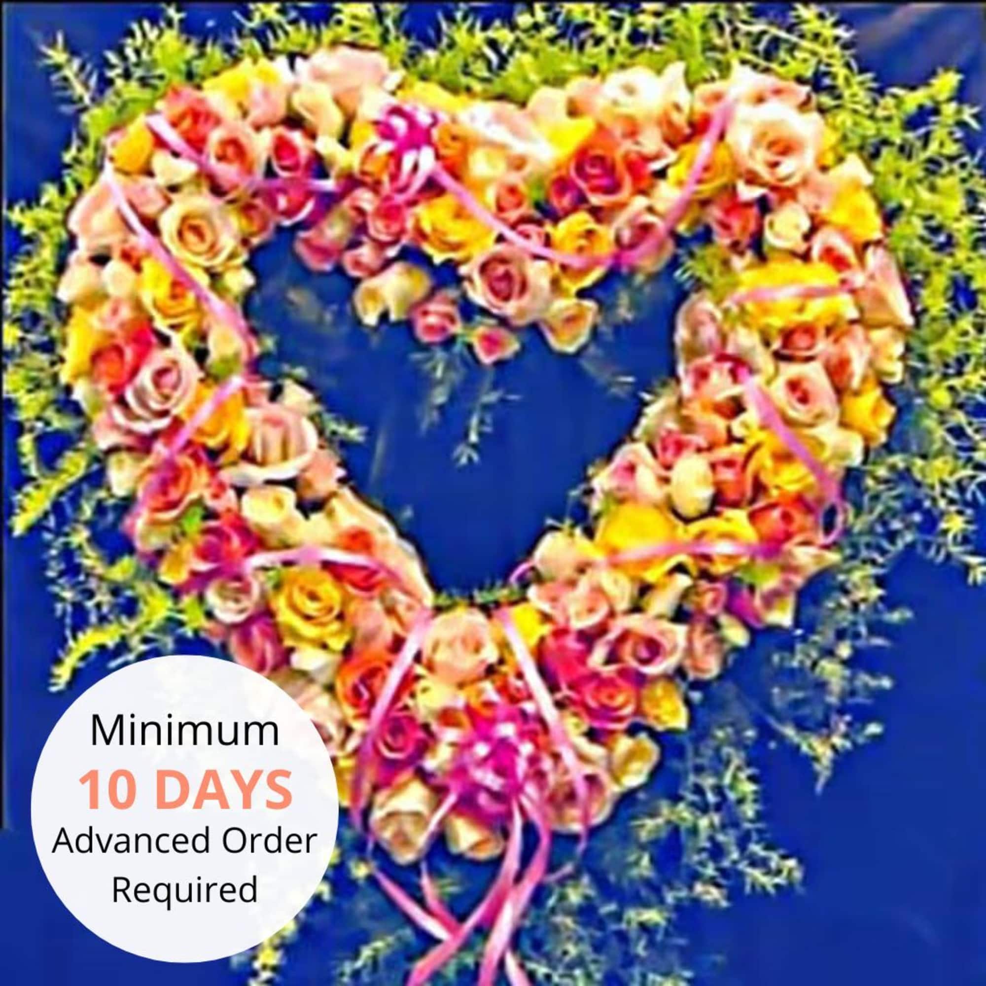 Heart-shaped wreath of pink and yellow roses with pink ribbons on a blue background.
