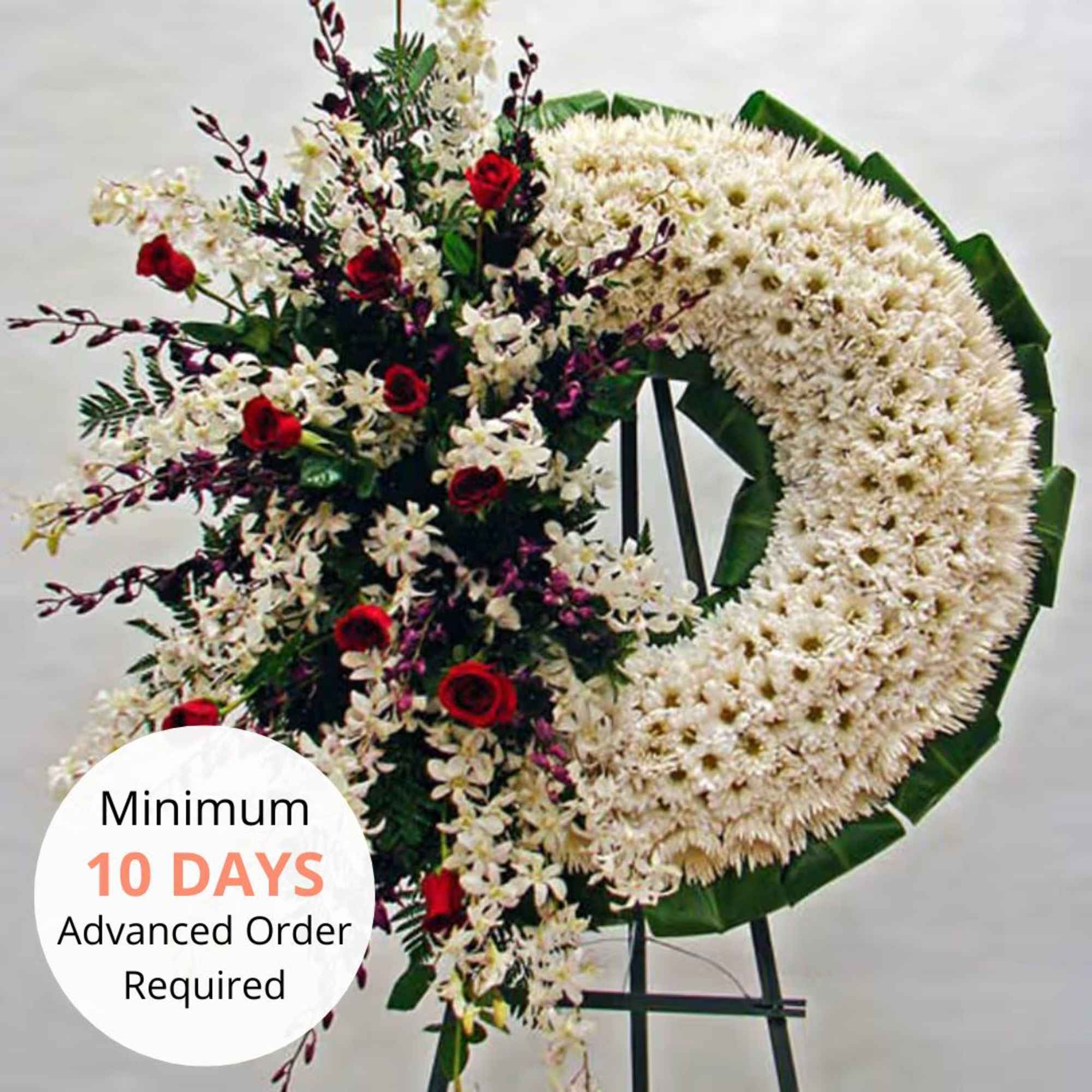 Large white floral wreath with red roses and orchids on a tall stand