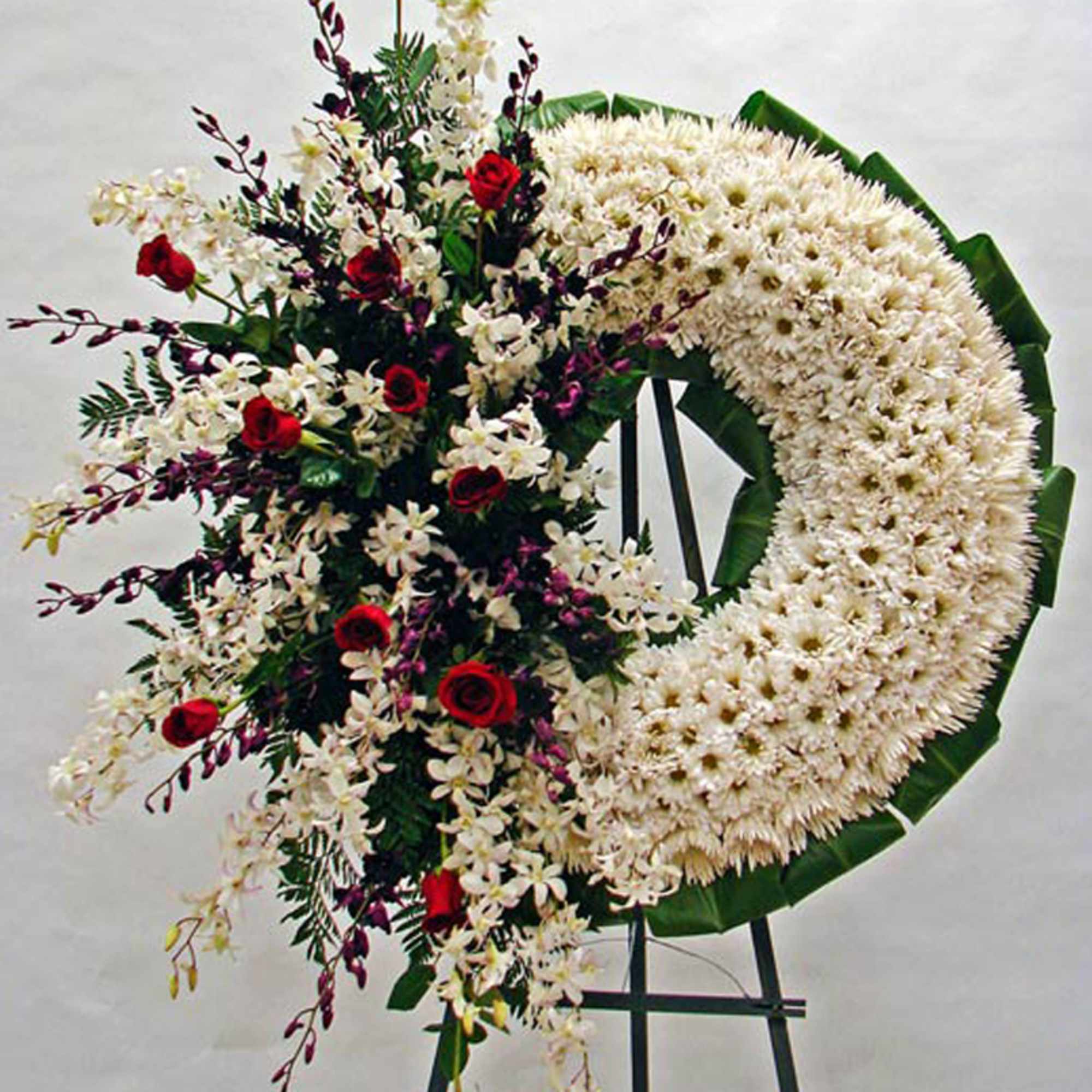 Standing white chrysanthemum wreath with cascading red roses and white orchids on an easel