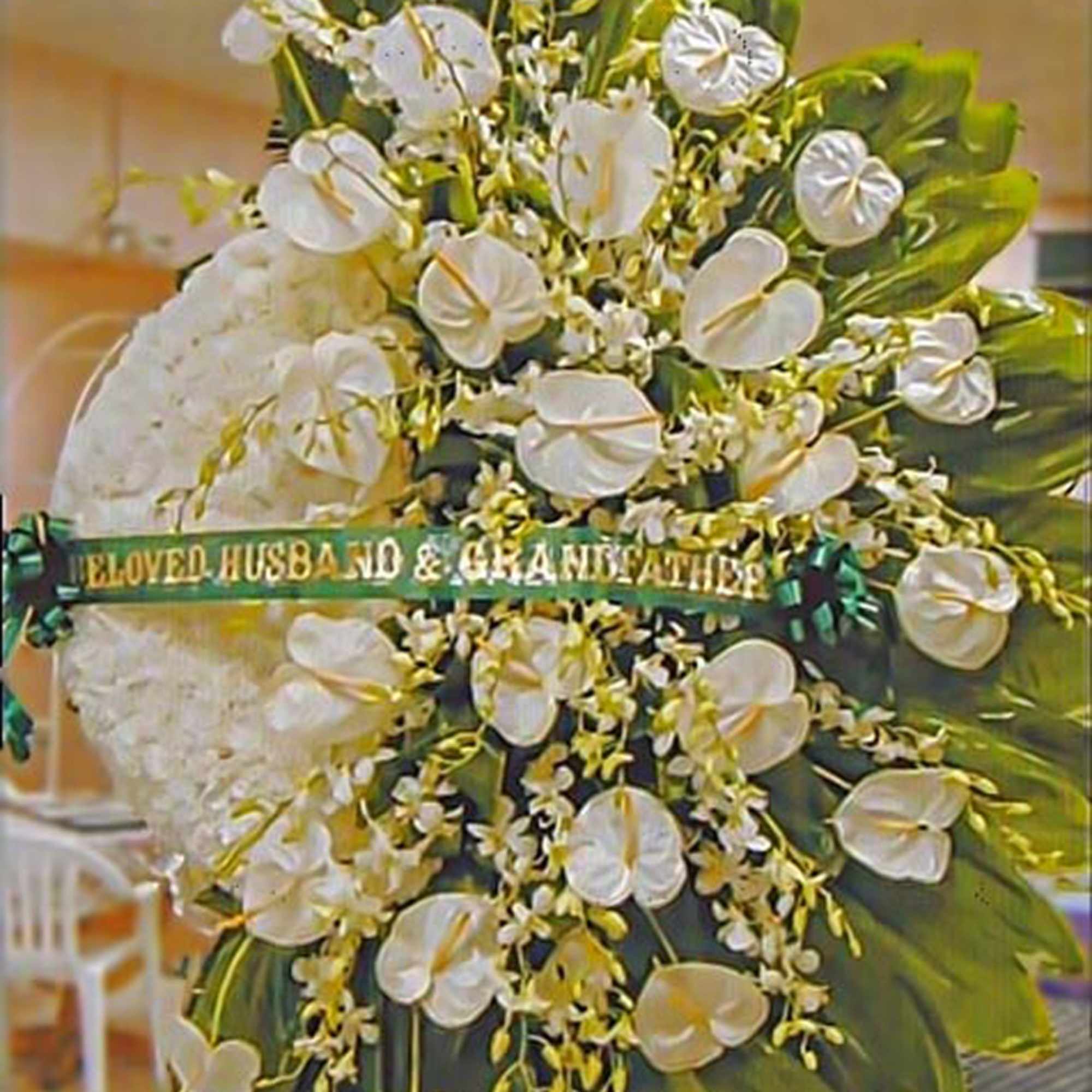 Standing funeral wreath of white flowers with green ribbon reading "Beloved Husband & Grandfather"