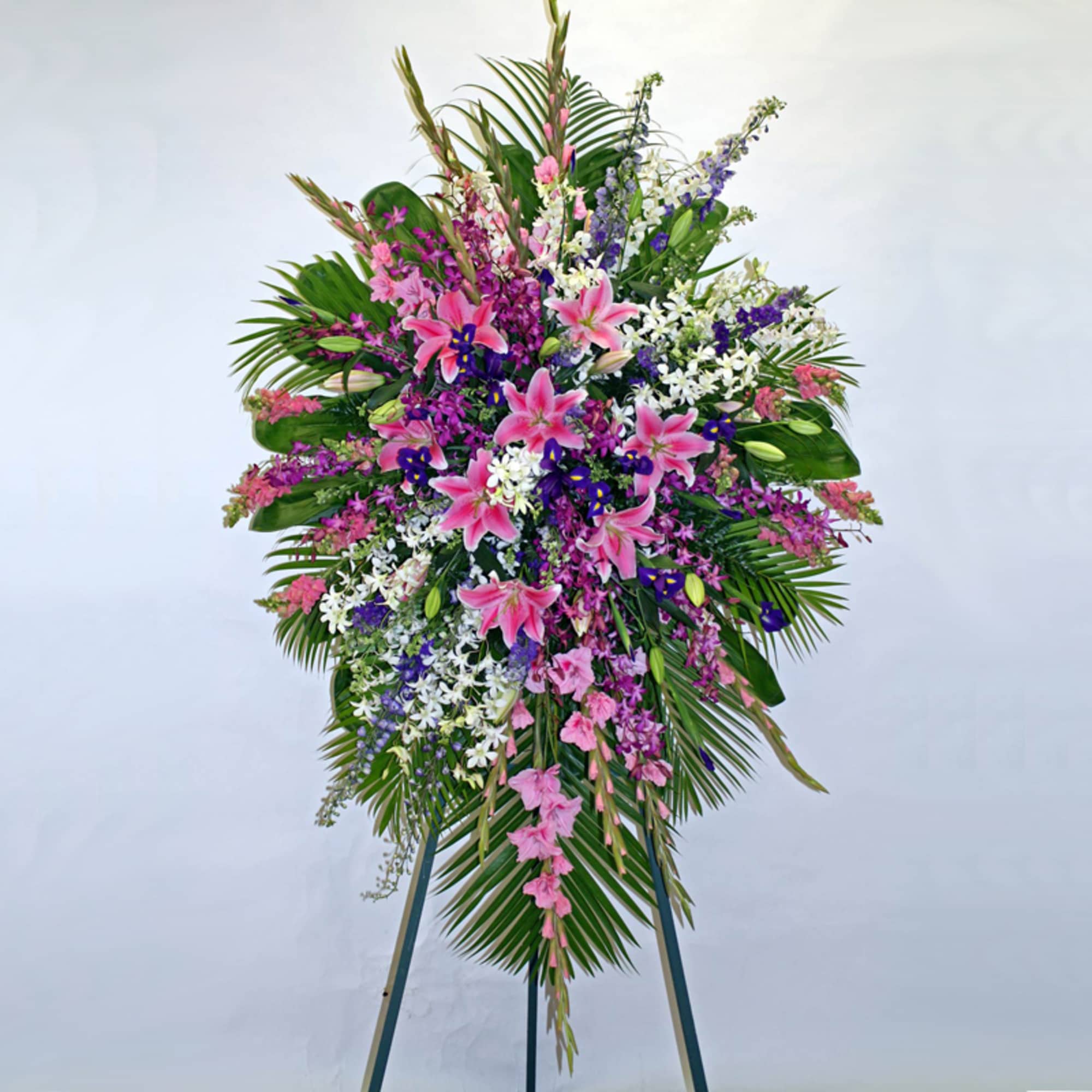 Tall standing spray of pink lilies, purple and white flowers on a metal easel.