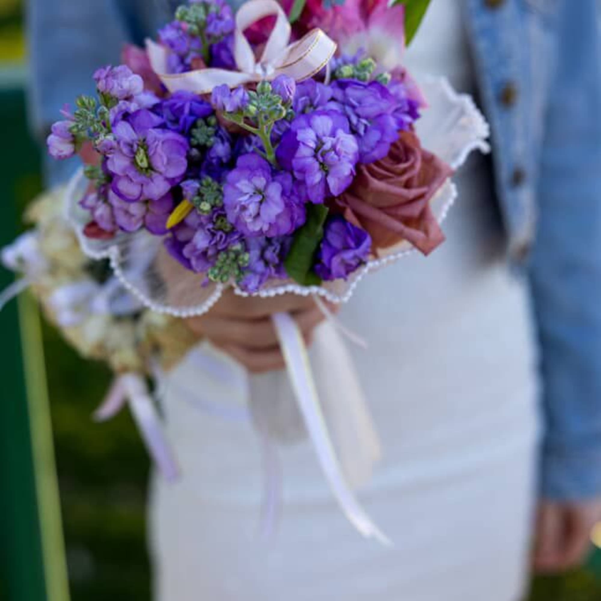 Handheld bouquet of purple and pink flowers with a ribbon
