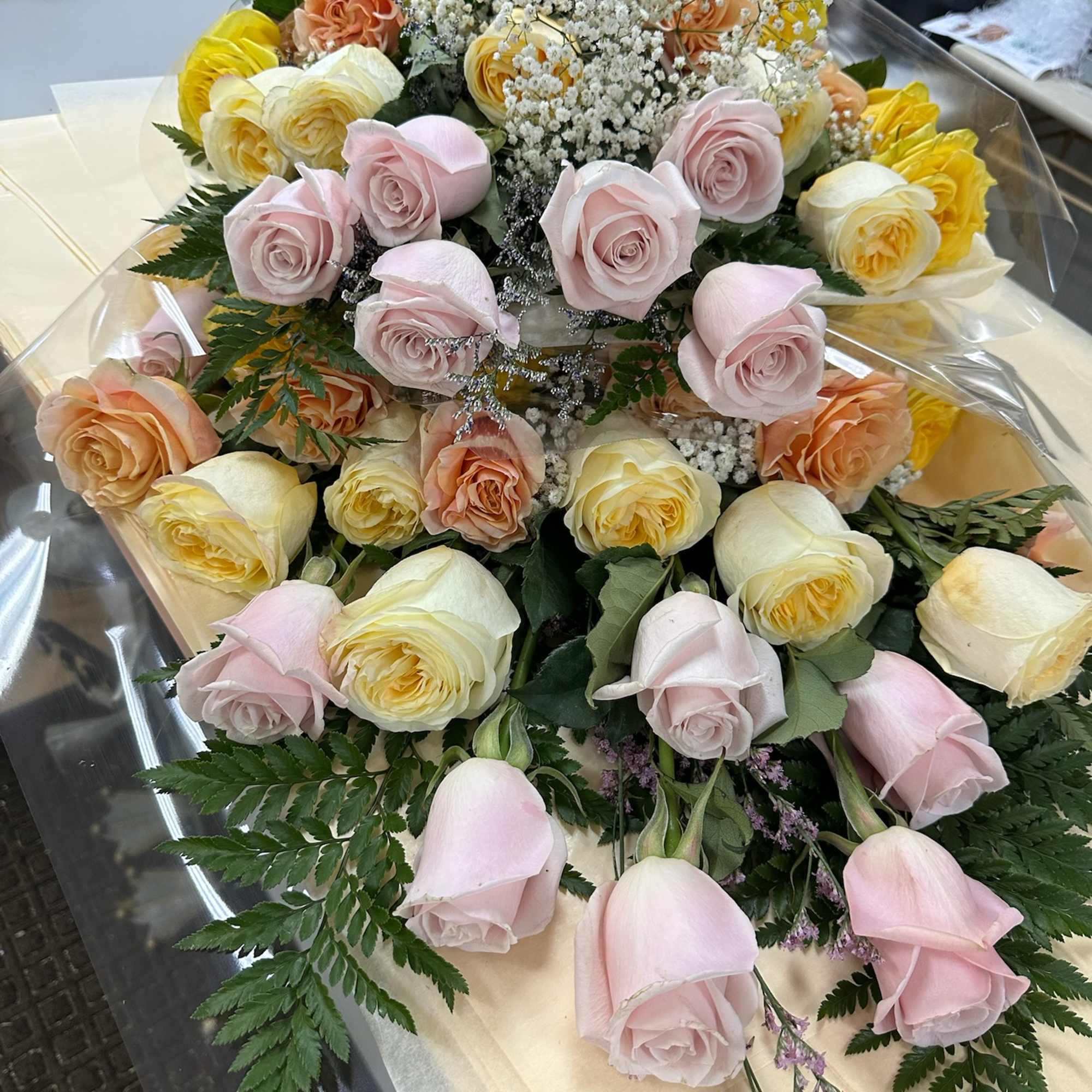 Bouquet of pastel roses with baby's breath and greenery in clear wrap
