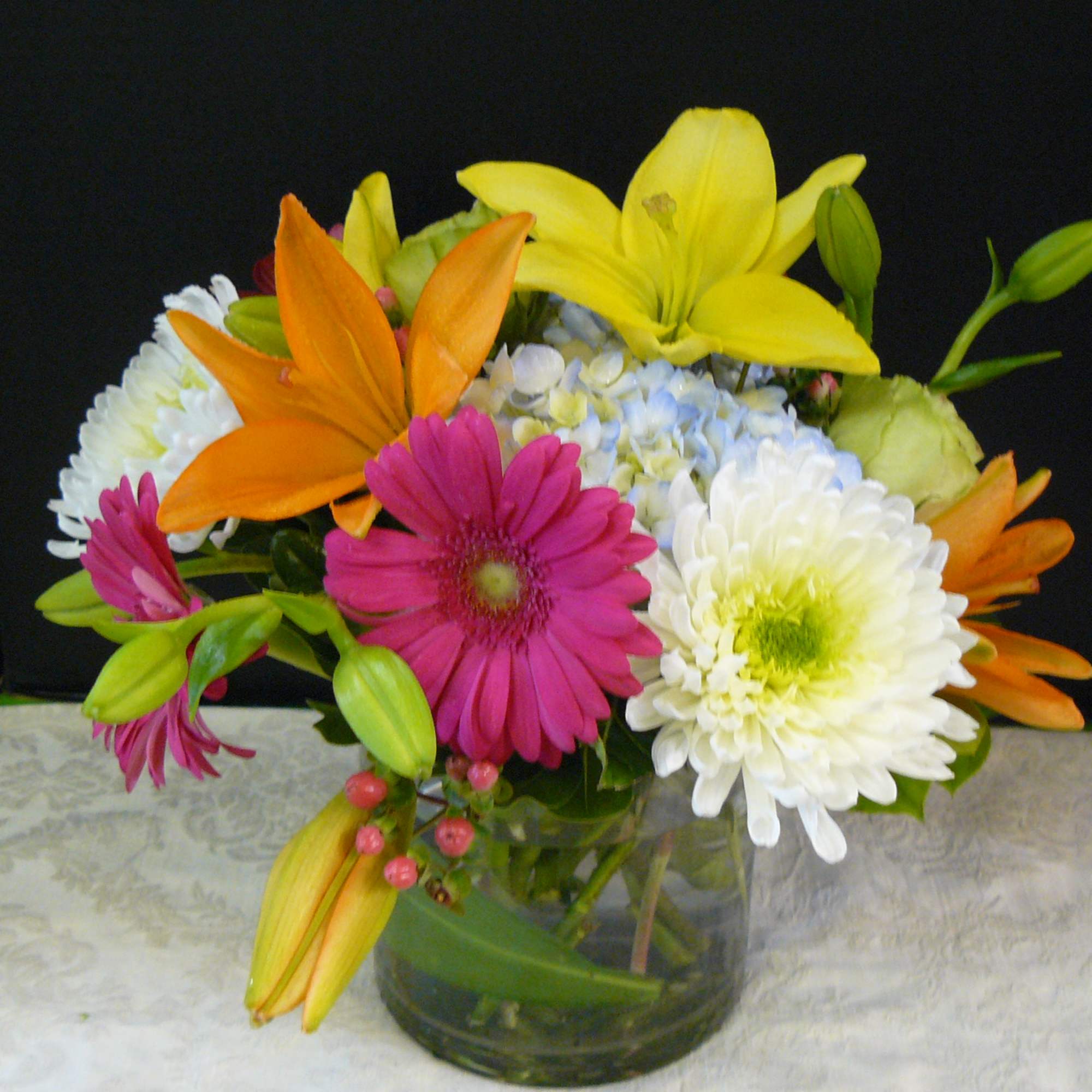 Mixed bouquet of lilies, daisies, and chrysanthemums in a glass vase