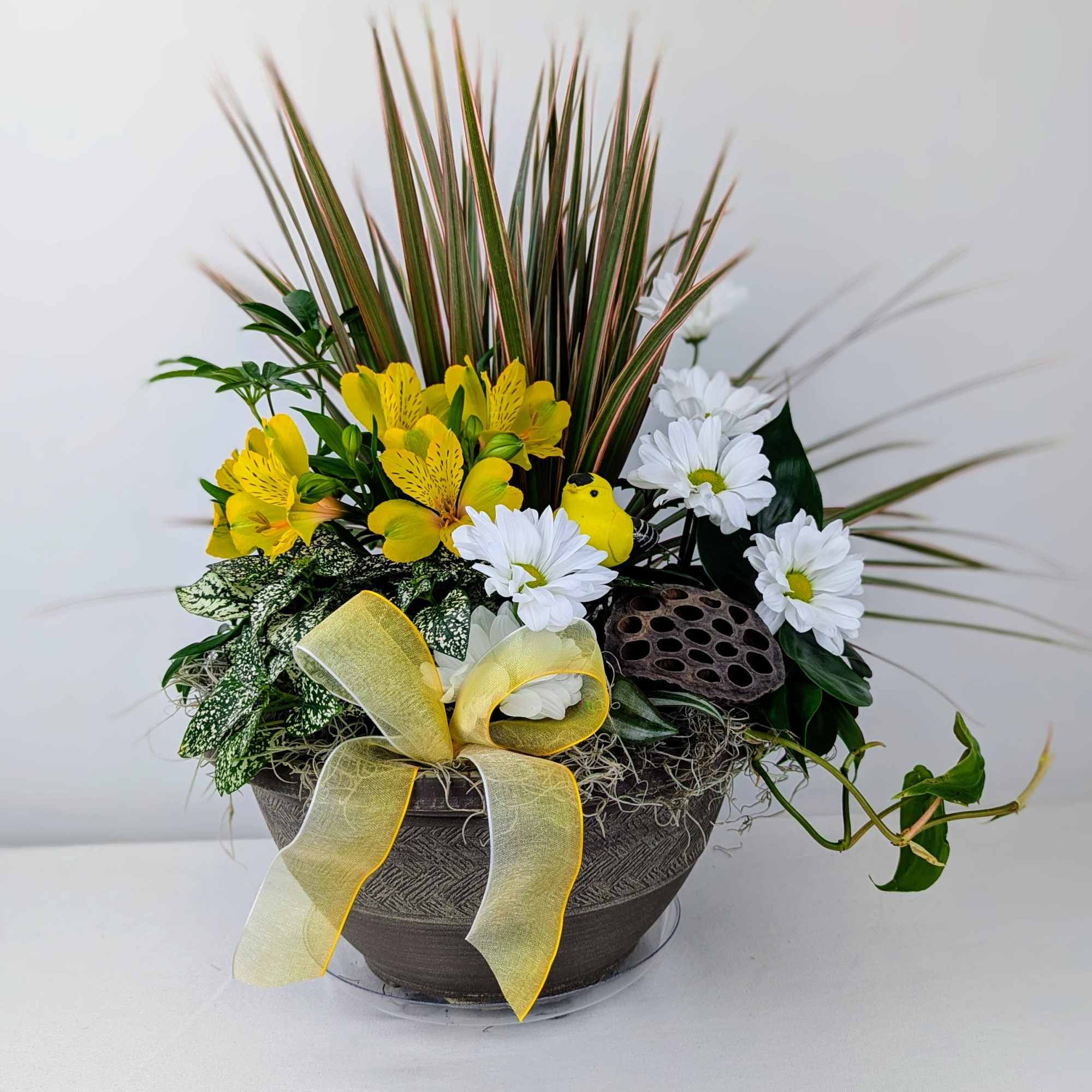 Yellow and white flowers in a gray bowl with a ribbon