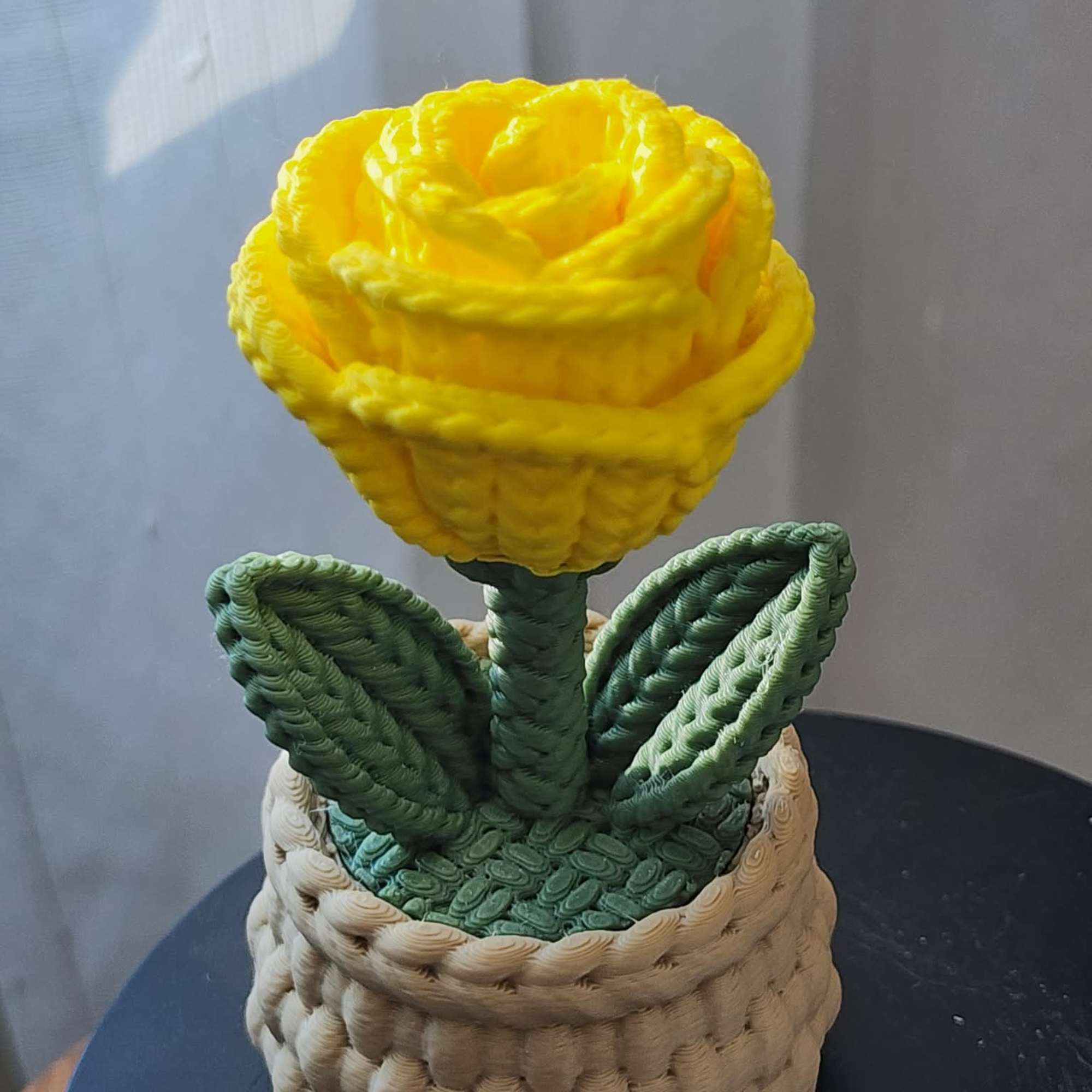 Yellow rose in a woven basket-style container with green leaves