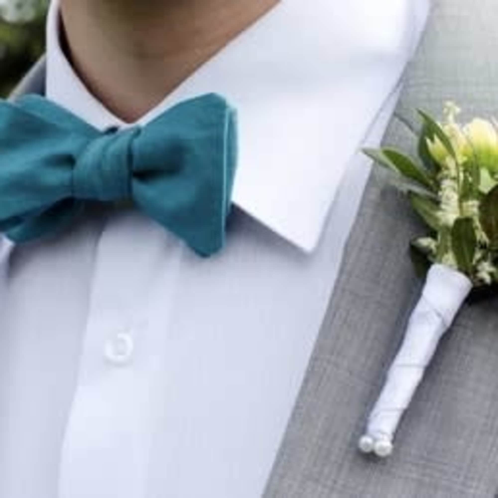 Gray suit with teal bow tie and a boutonniere with white flowers