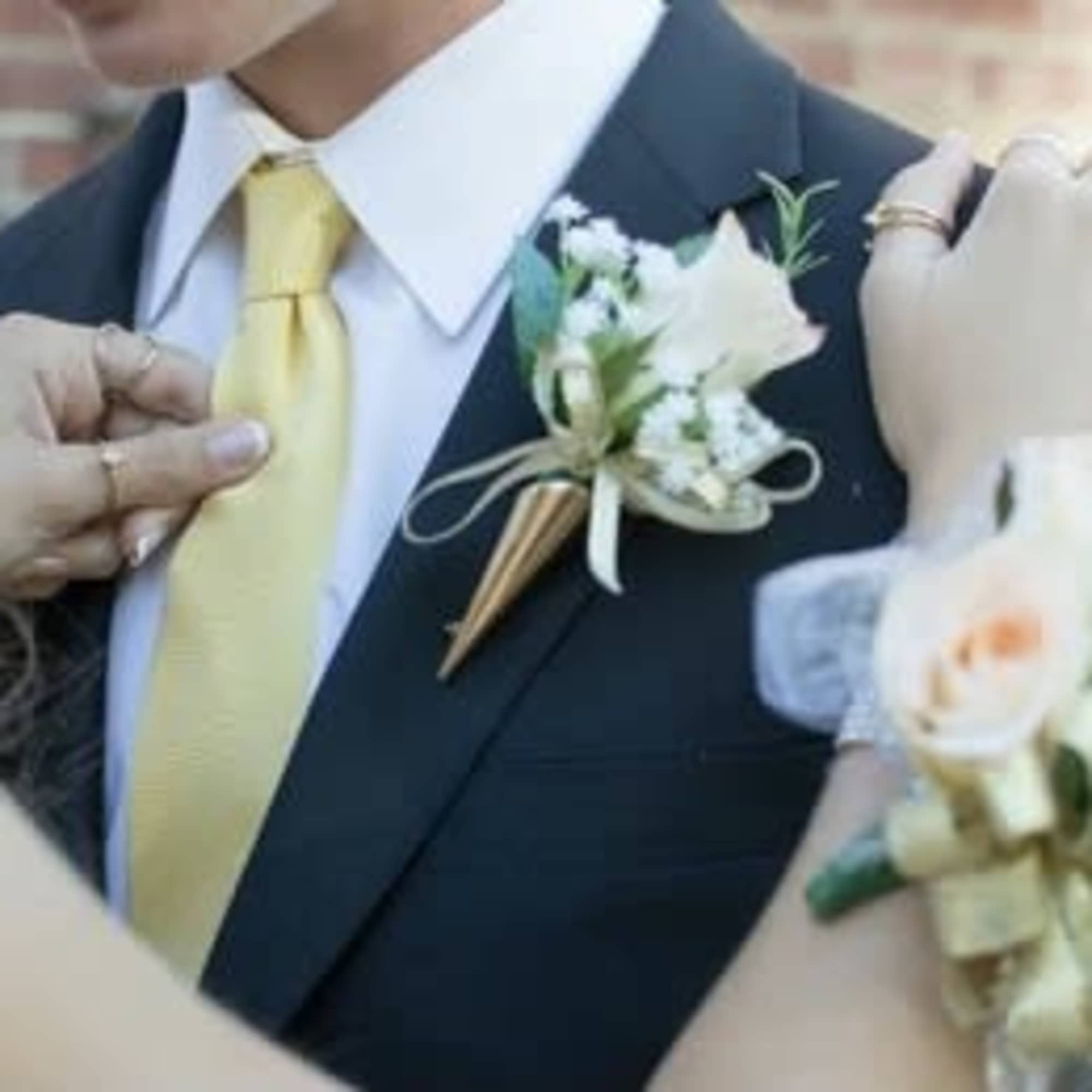 White boutonniere pinned to a suit jacket beside a yellow tie