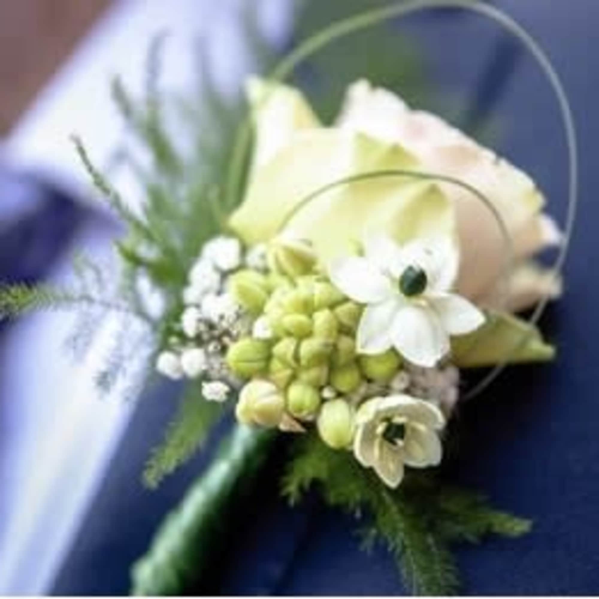 Small white boutonniere with pale green accents pinned to a suit jacket