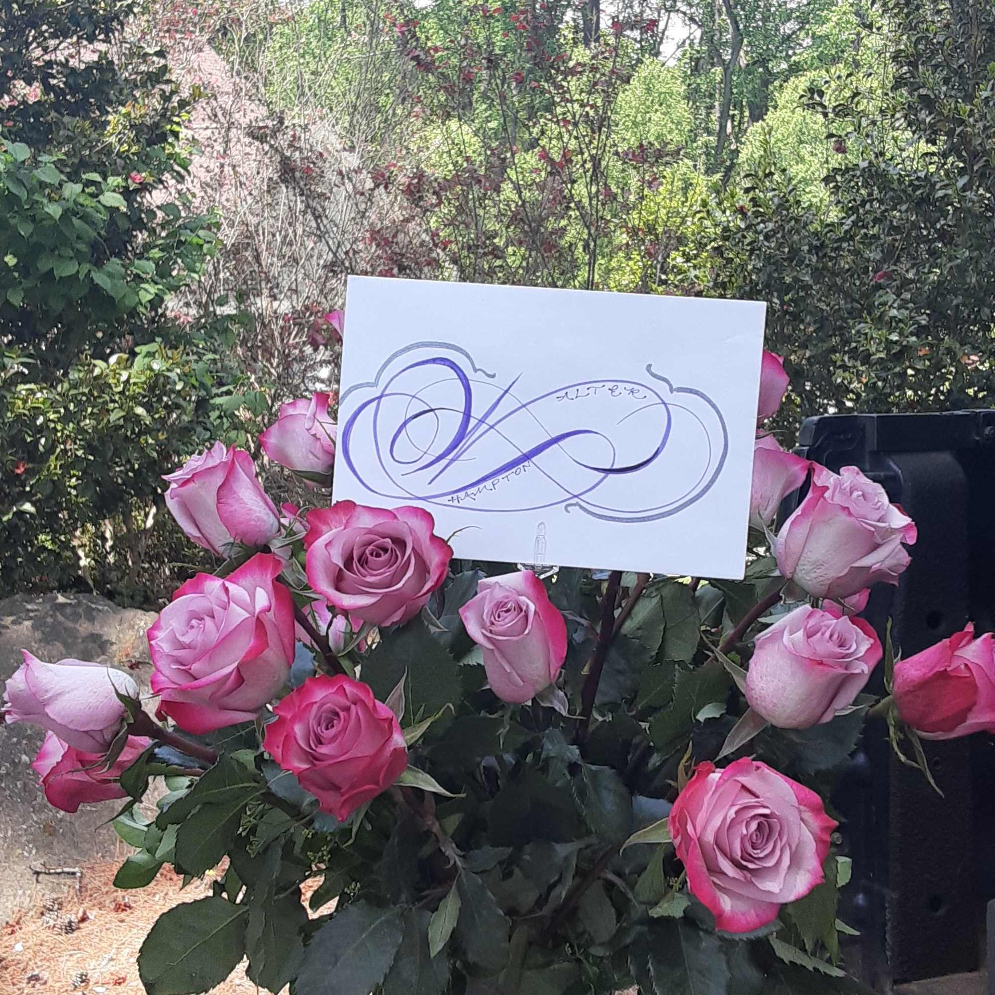 Pink roses arranged in a clear glass vase with a card tucked in front
