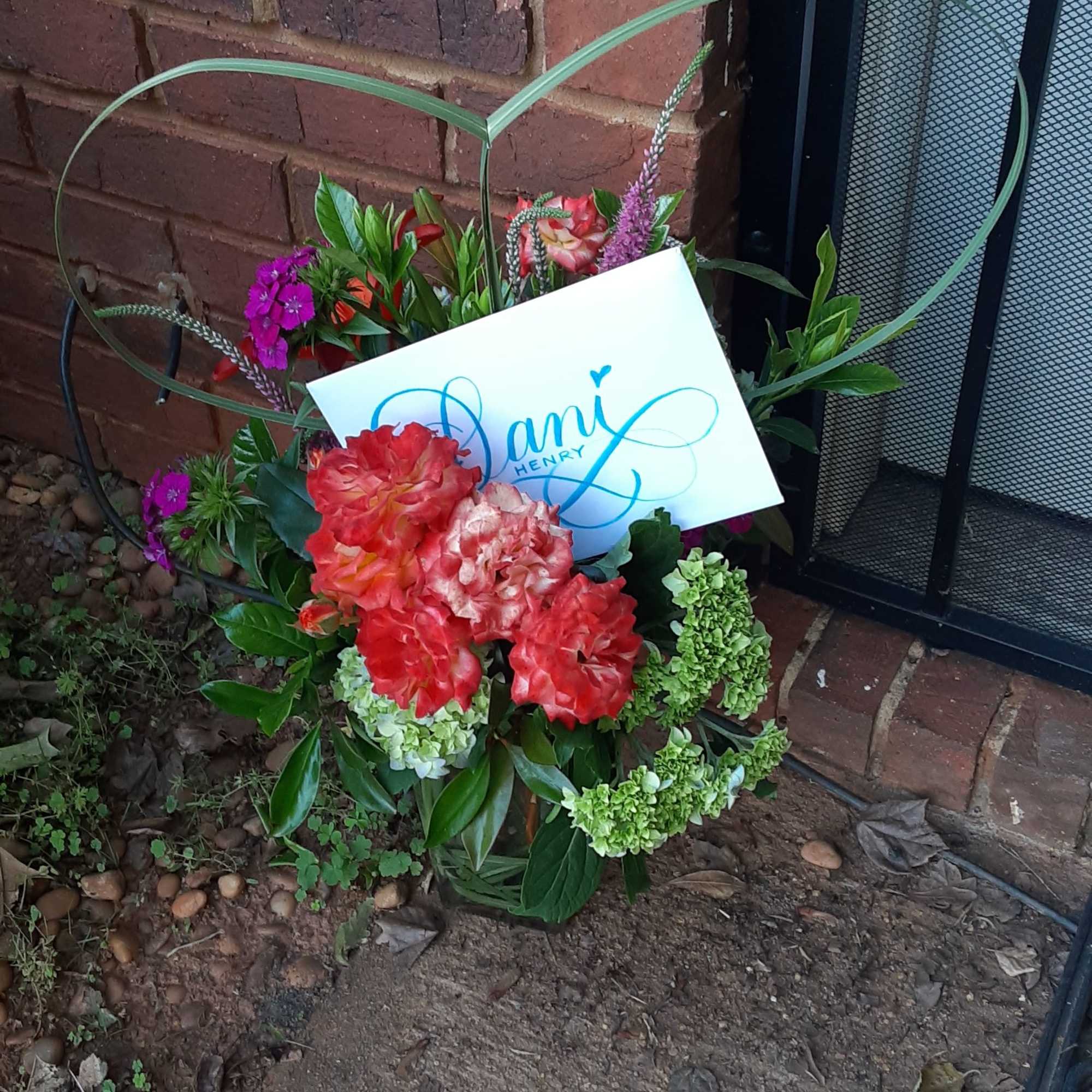 Floral arrangement with red and pink blooms and a name card in a heart-shaped frame