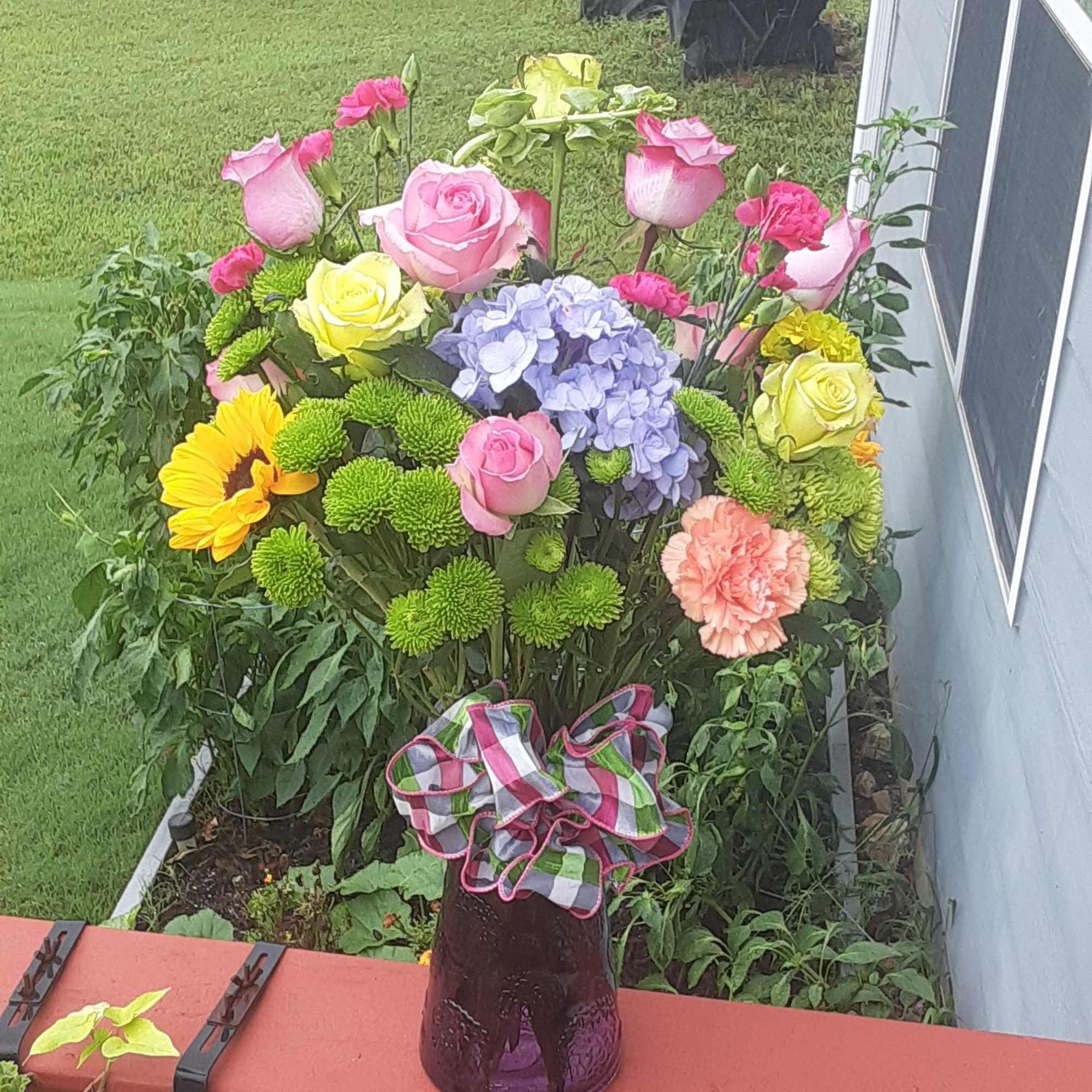 Mixed bouquet in a purple glass vase with a plaid ribbon