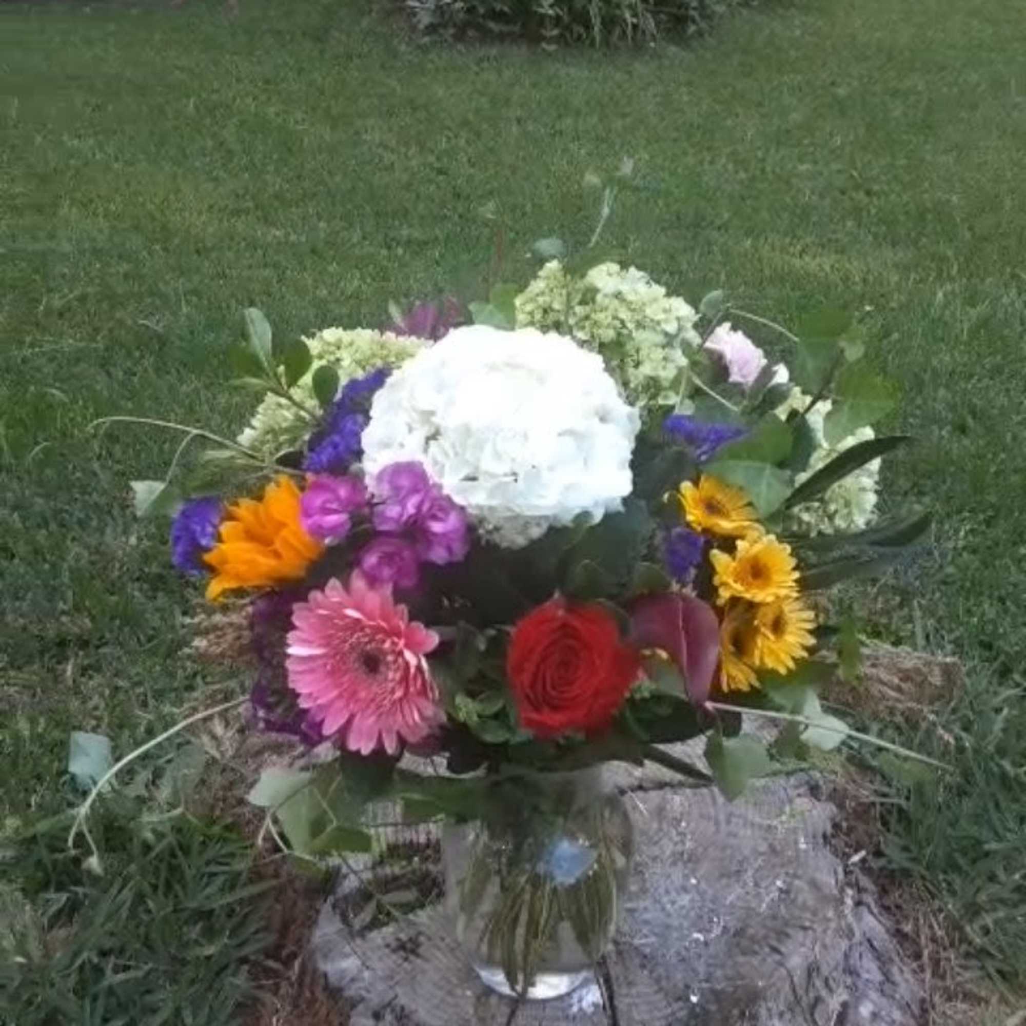 Colorful mixed bouquet in a clear glass vase on a tree stump