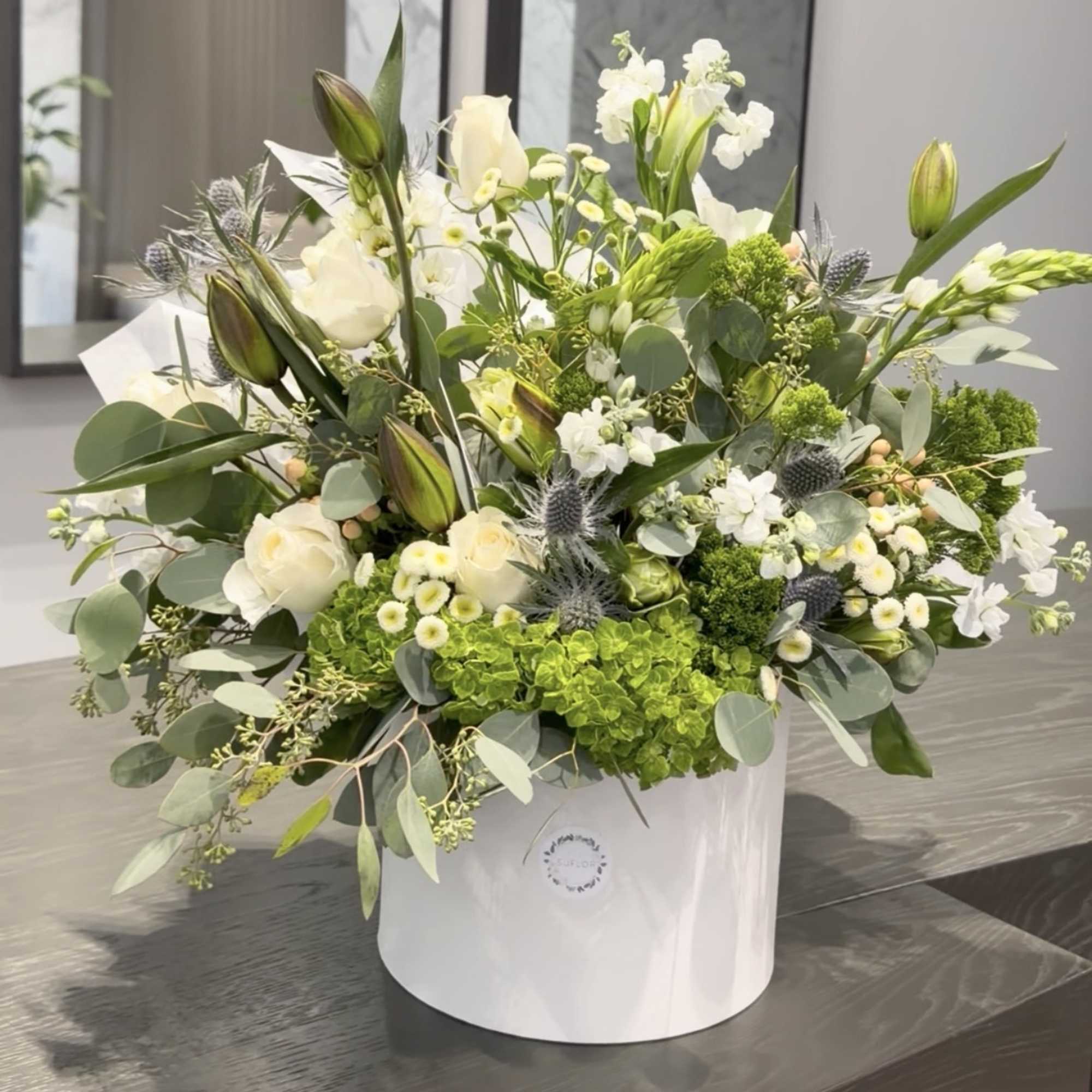 White and green floral arrangement in a white hat box