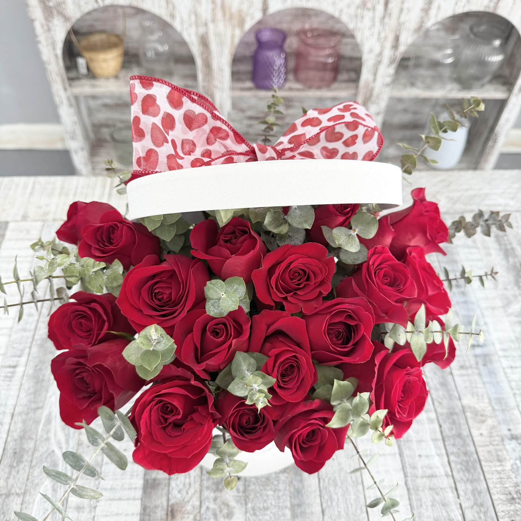 Red roses in a white box with a heart-patterned bow