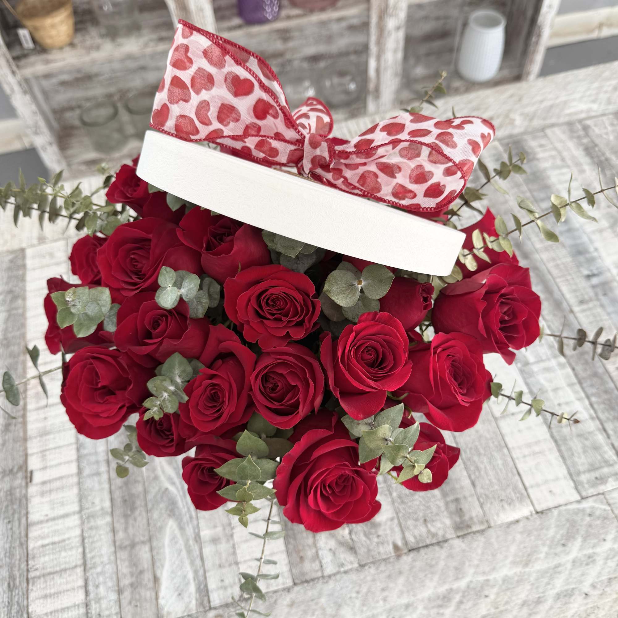 Red roses in a white hat box with a heart-patterned ribbon