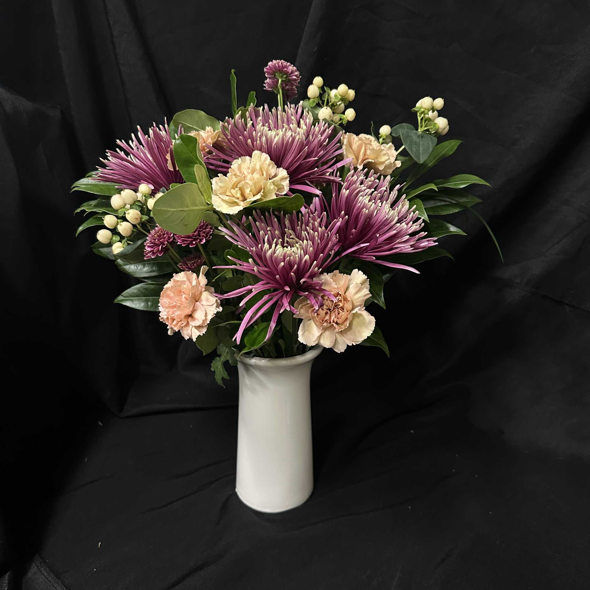 Purple chrysanthemums and peach carnations in a white vase