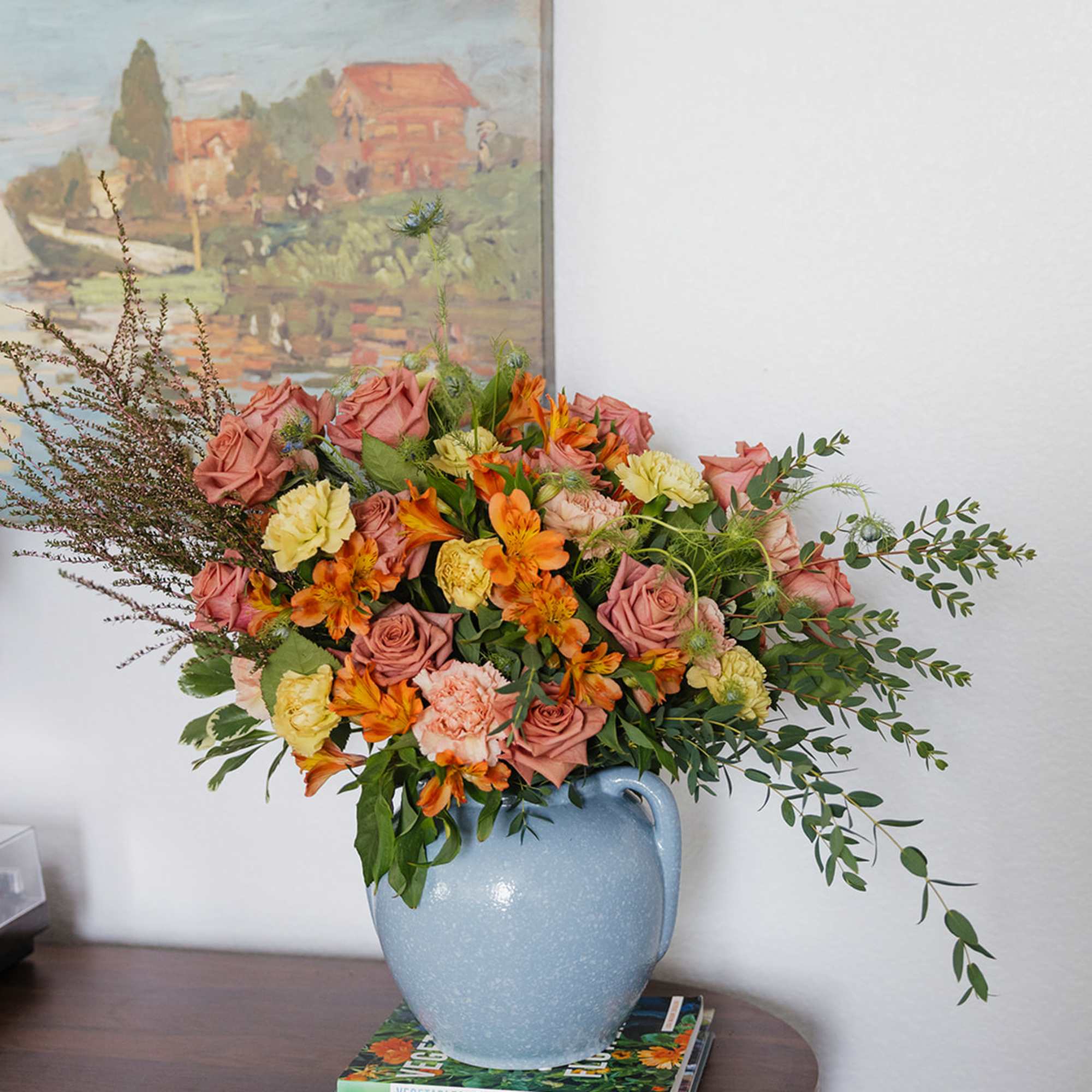 Bouquet of pink roses, orange alstroemeria, and yellow carnations in a blue vase