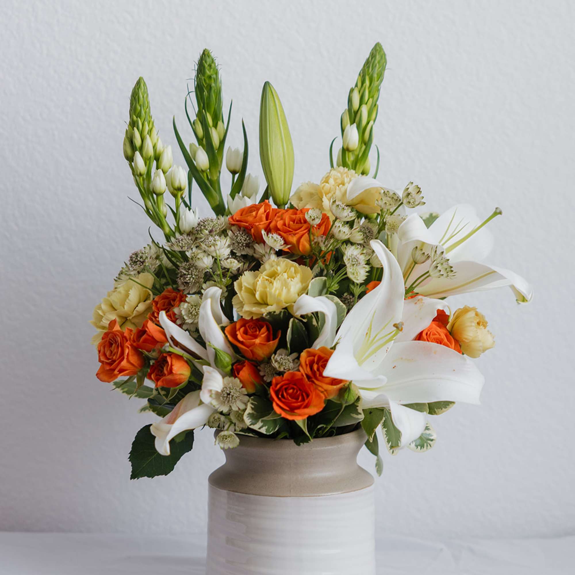 Orange roses and white lilies arranged in a ceramic vase