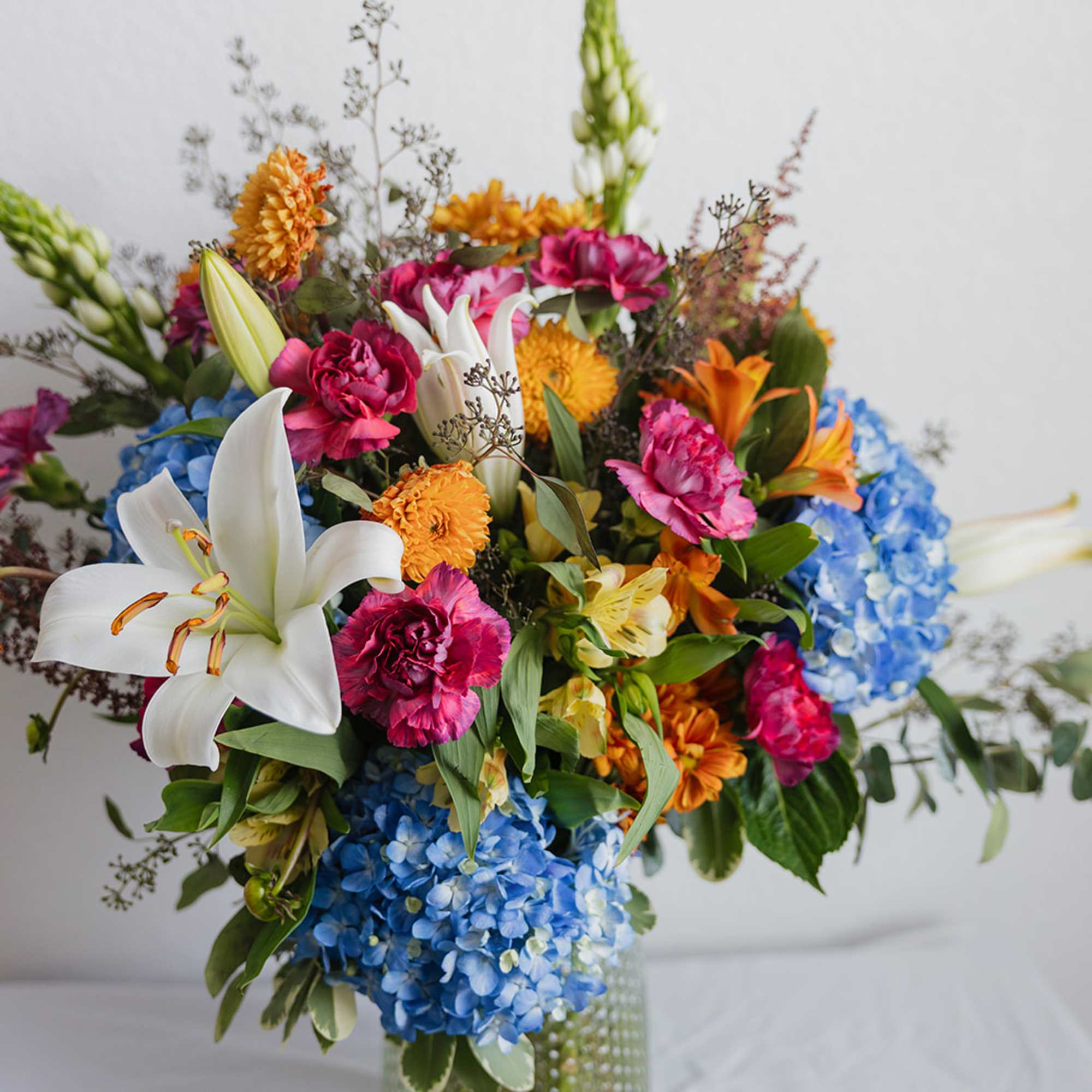 Mixed bouquet with white lilies, blue hydrangeas, and pink and orange flowers