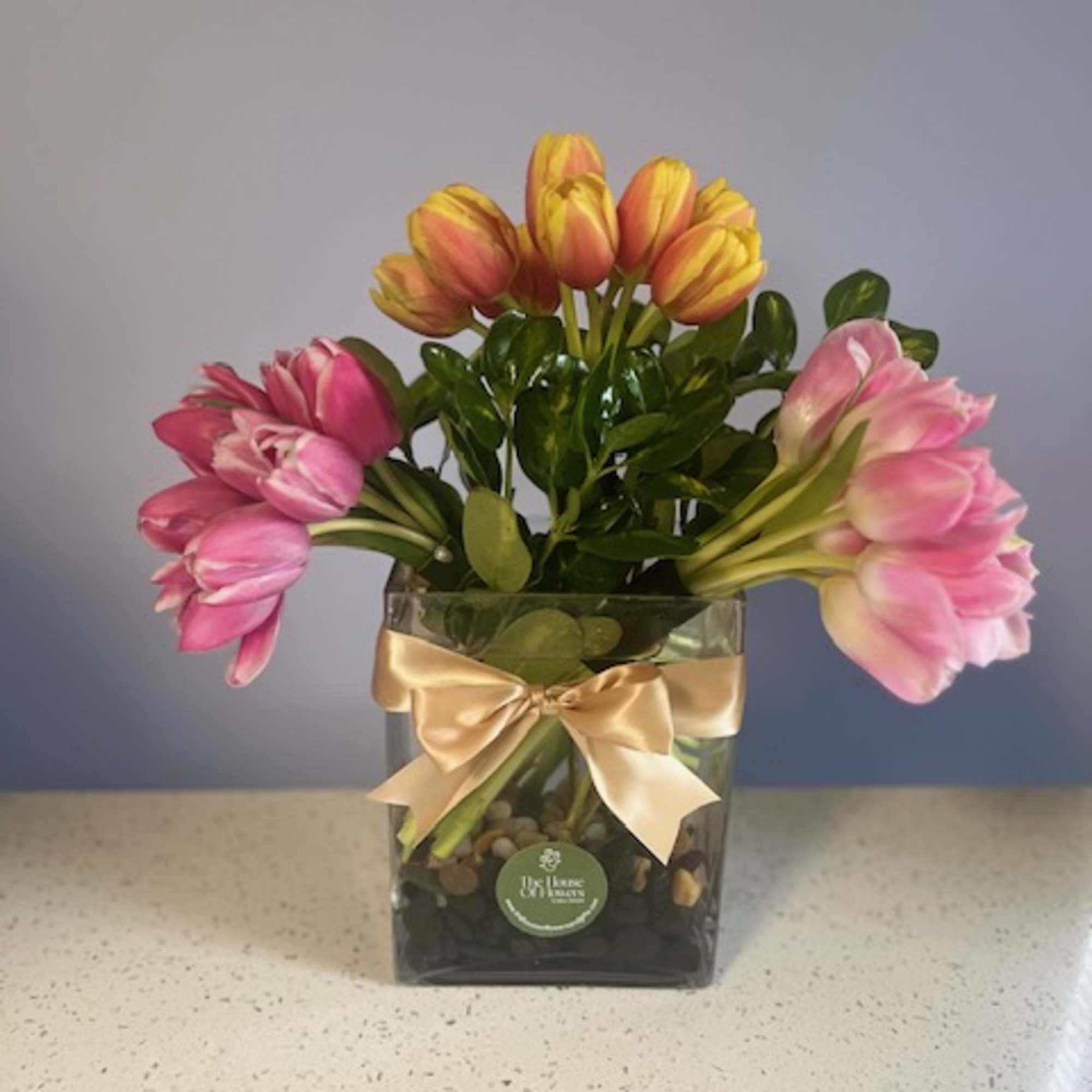 Pink and yellow tulips in a square glass vase with a gold ribbon